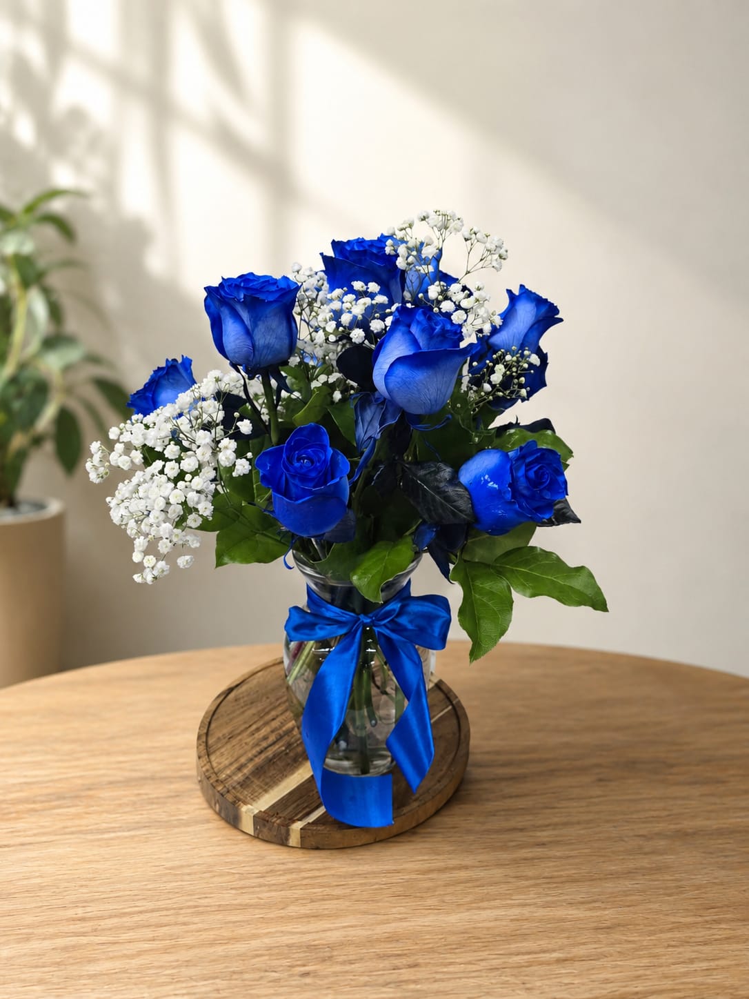 Blue roses and white baby's breath in a glass vase with a blue ribbon
