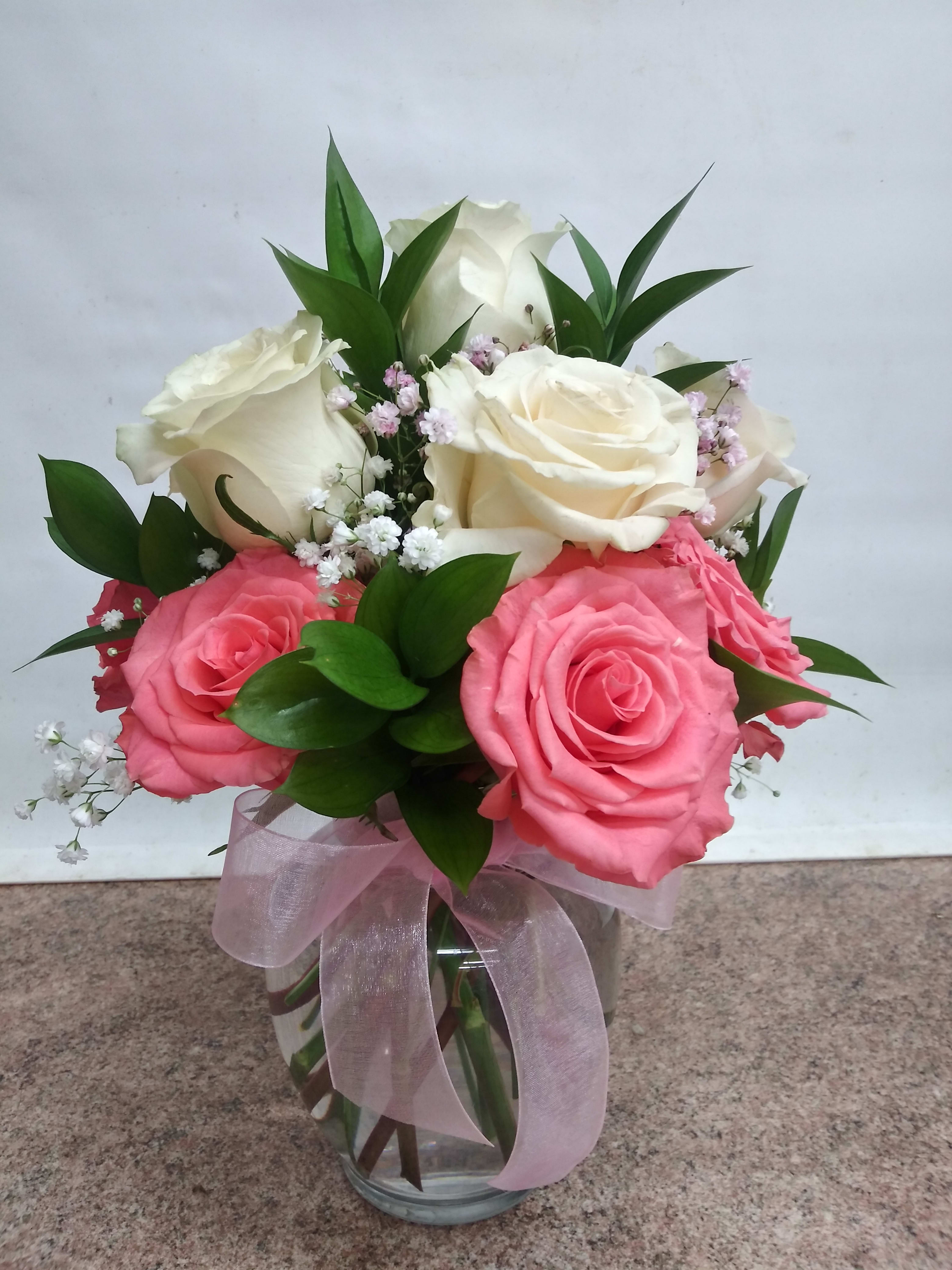 Pink and white roses arranged in a glass vase with a pink ribbon