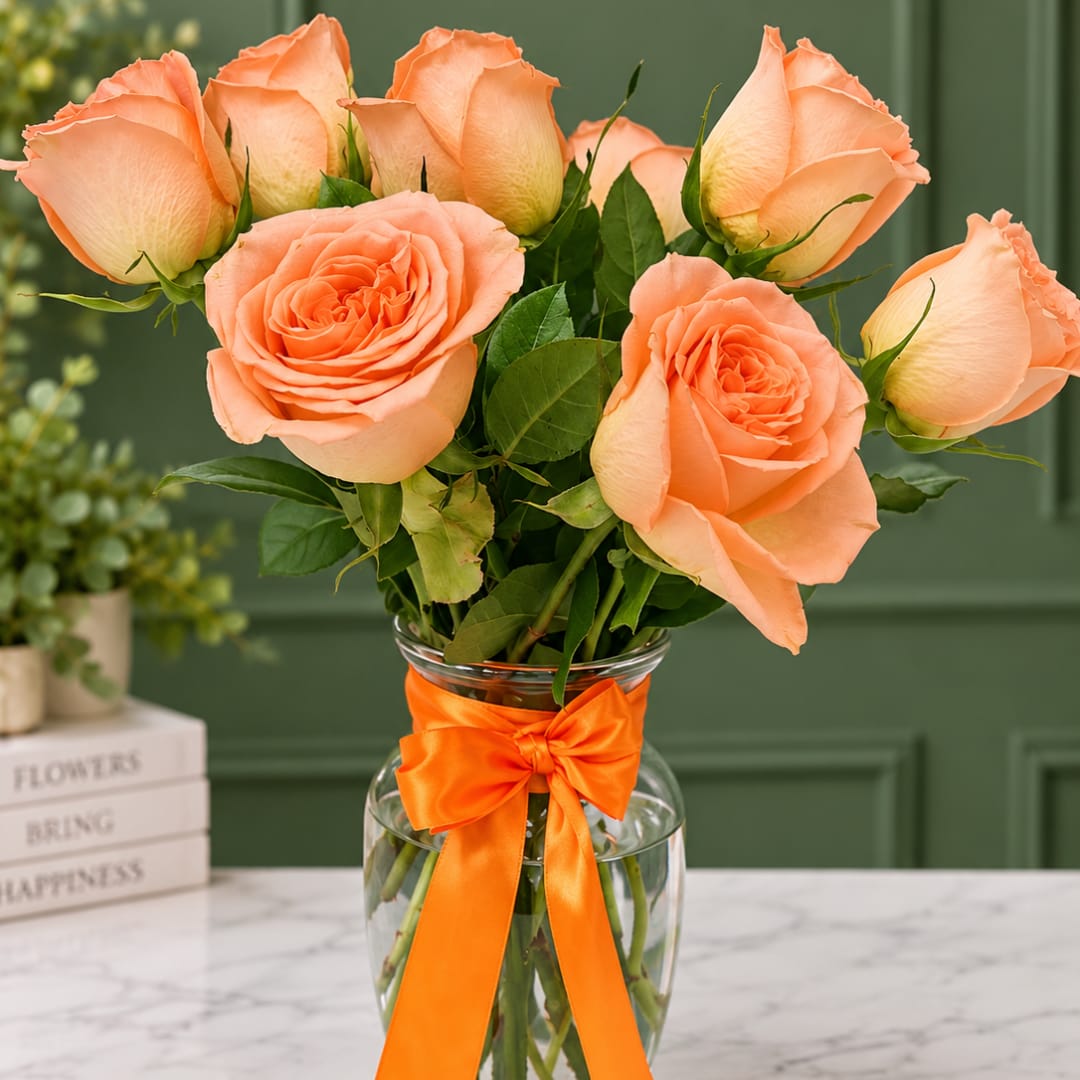 Peach roses in a clear glass vase with an orange ribbon