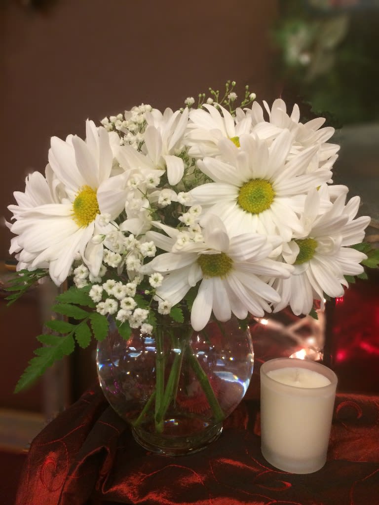 White daisy bouquet in a glass vase with a small candle beside it