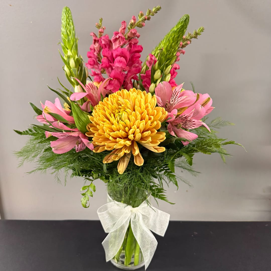 Pink and yellow mixed bouquet in a clear glass vase with a white bow
