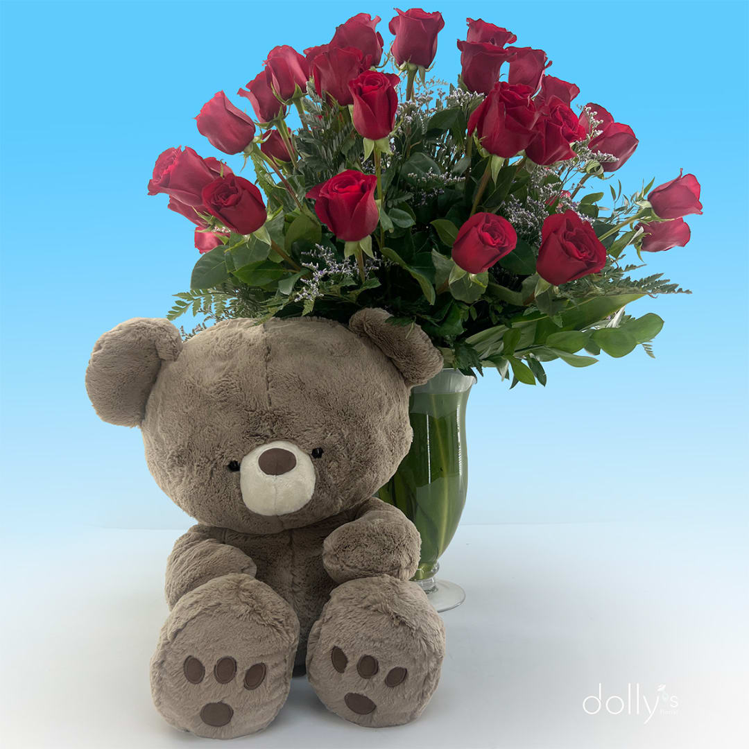Red roses in a glass vase with a plush teddy bear in front