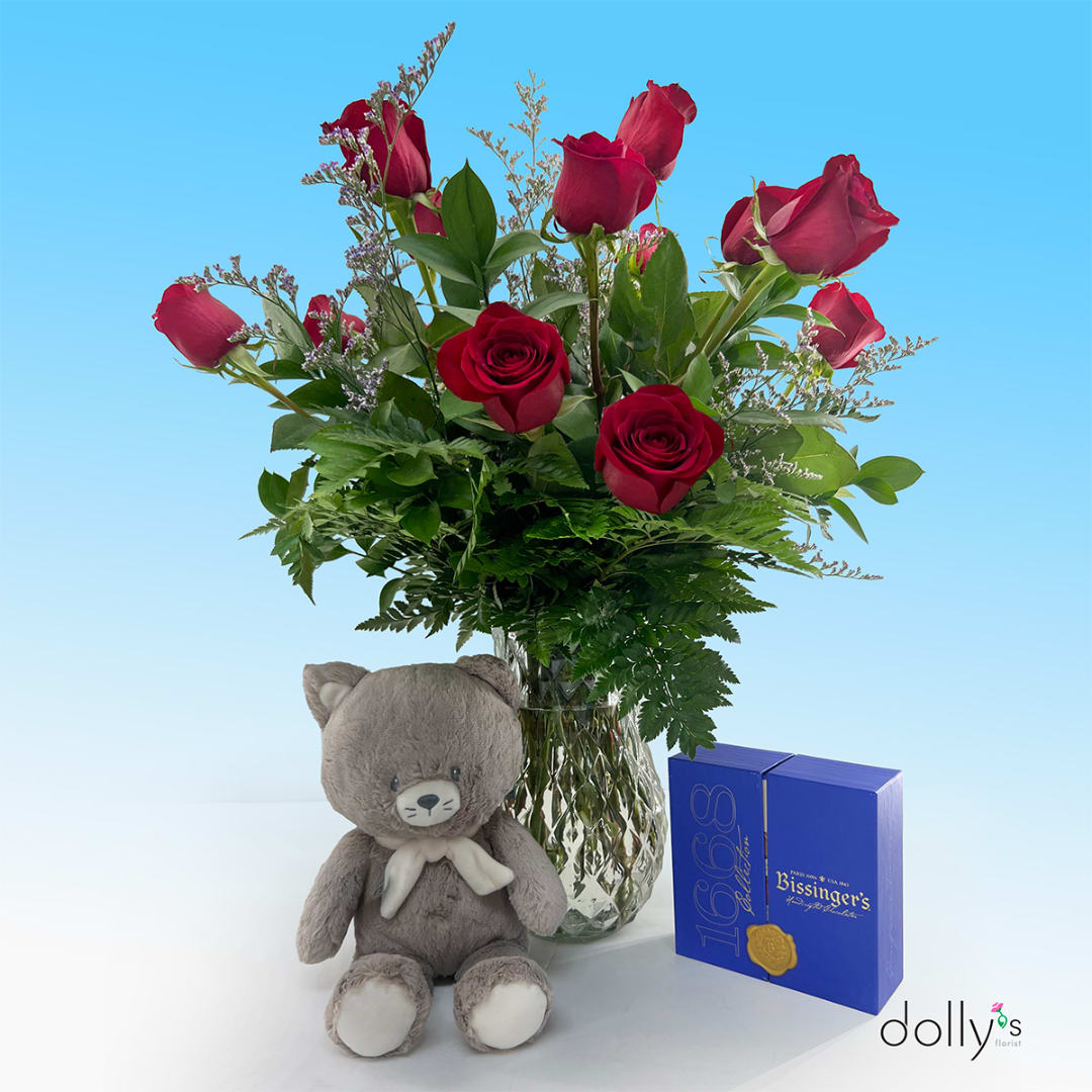 Red roses in a glass vase with a teddy bear and chocolate box