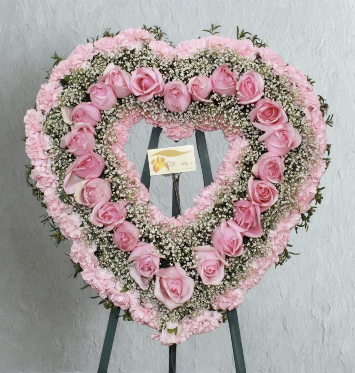 Heart-shaped pink rose and carnation floral wreath on an easel