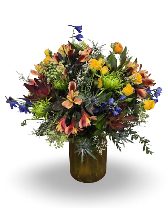 Antiquity - Select this garden-style arrangement bursting with warm sunset tones, pops of blue and playful texture throughout. Designed in a vase with greenery and unique seasonal blooms Approx. 19" x 17"