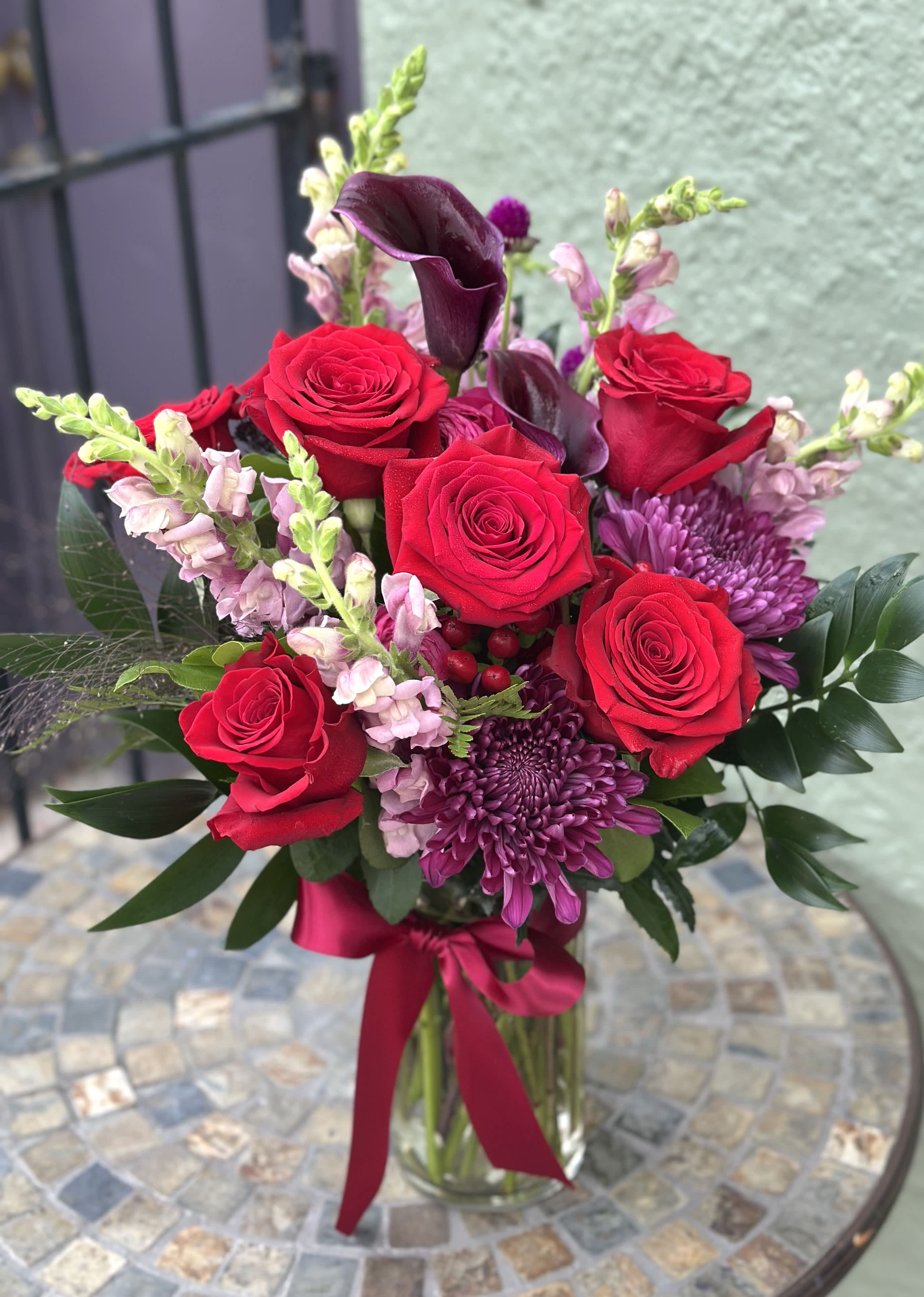 Bouquet of red roses and purple flowers in a glass vase with a ribbon