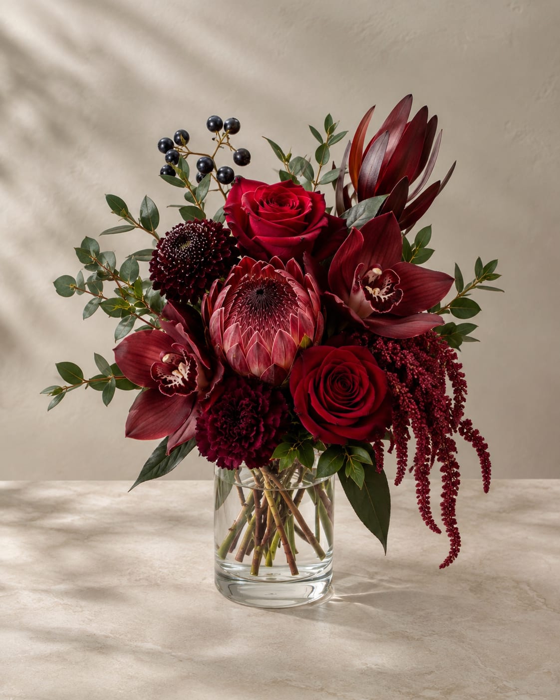 Deep red bouquet in a clear glass vase with roses and tropical blooms