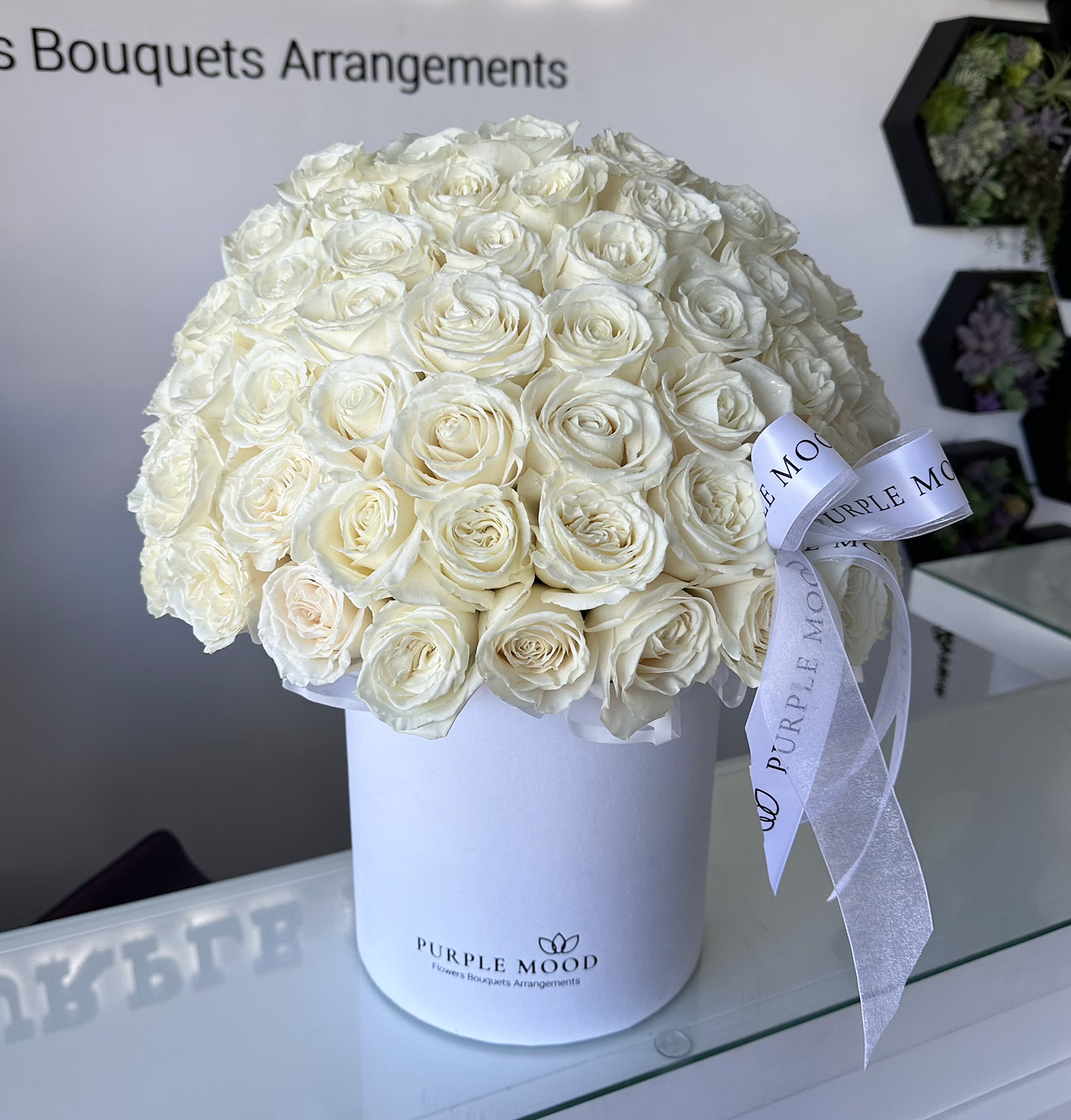 50 White Roses In a Box - Available Sizes:     •    STANDARD - 50 roses (Container size D8.25'x H9.5')     •    DELUXE - 100 roses (Container size D10.5'x H12.25')  Premium white roses in a box. Elegant, timeless, and full of grace — our 50 White Roses in Box arrangement is a breathtaking display of purity and sophistication. Each rose is carefully hand-selected and arranged into a flawless dome inside our signature velvet hatbox, finished with a satin ribbon. White roses symbolize respect, admiration, and eternal love, making this the perfect gift for weddings, anniversaries, or moments that call for a refined expression of emotion.   •    50 premium white roses beautifully arranged in a luxury hatbox     •    Represents purity, respect, and everlasting love     •    Wrapped with a satin ribbon for a sophisticated finish     •    Ideal for weddings, anniversaries, sympathy, or luxury gifting
