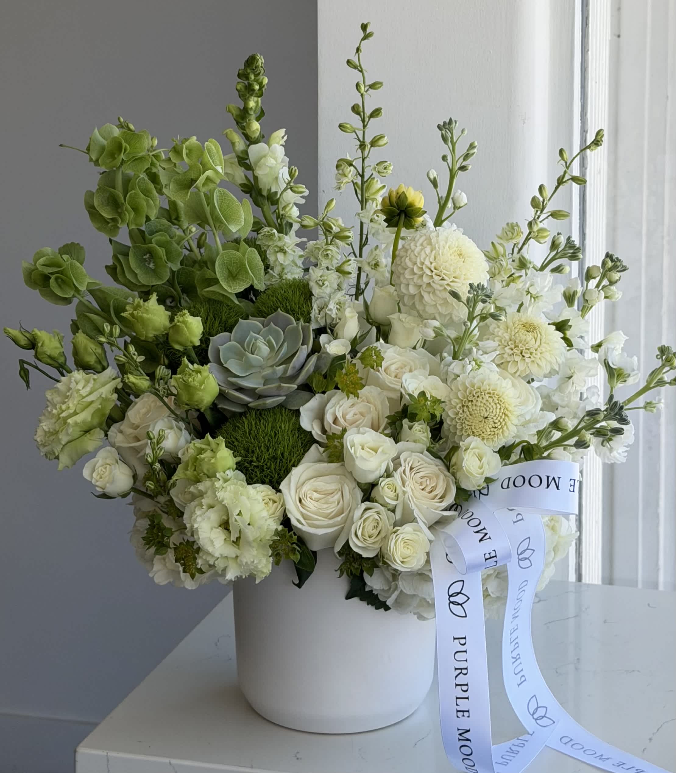 White and green floral arrangement in a white hatbox with a ribbon