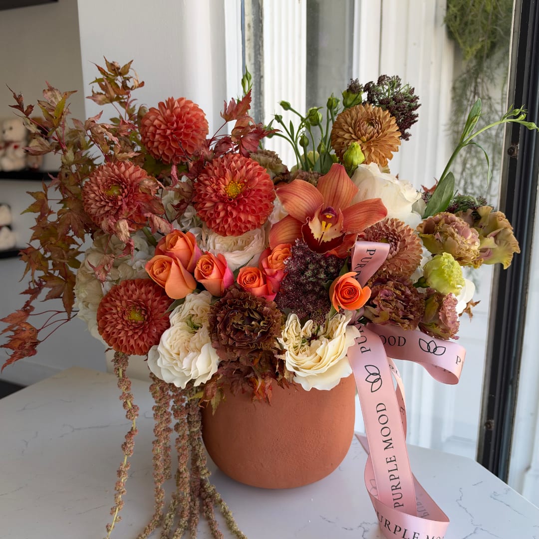 Orange and cream floral arrangement in a terracotta vase with a pink ribbon