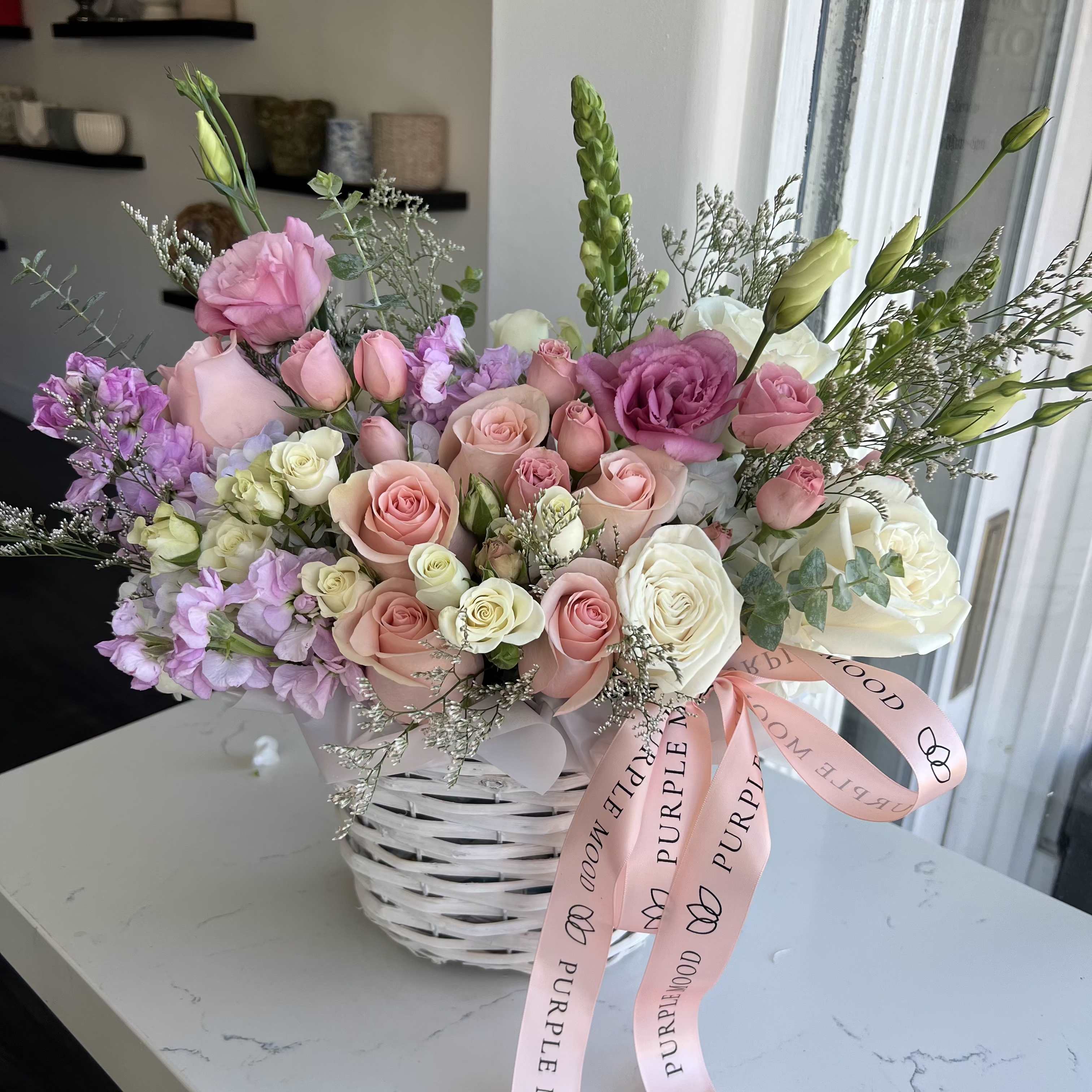 Pink and white rose bouquet in a white basket with a pink ribbon