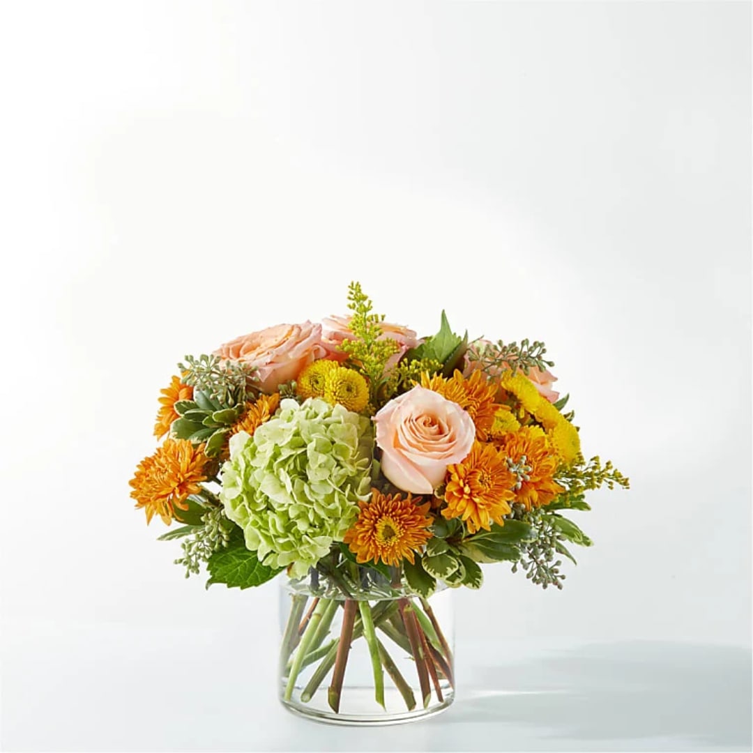 Peach roses and orange mums in a clear glass vase with green hydrangea
