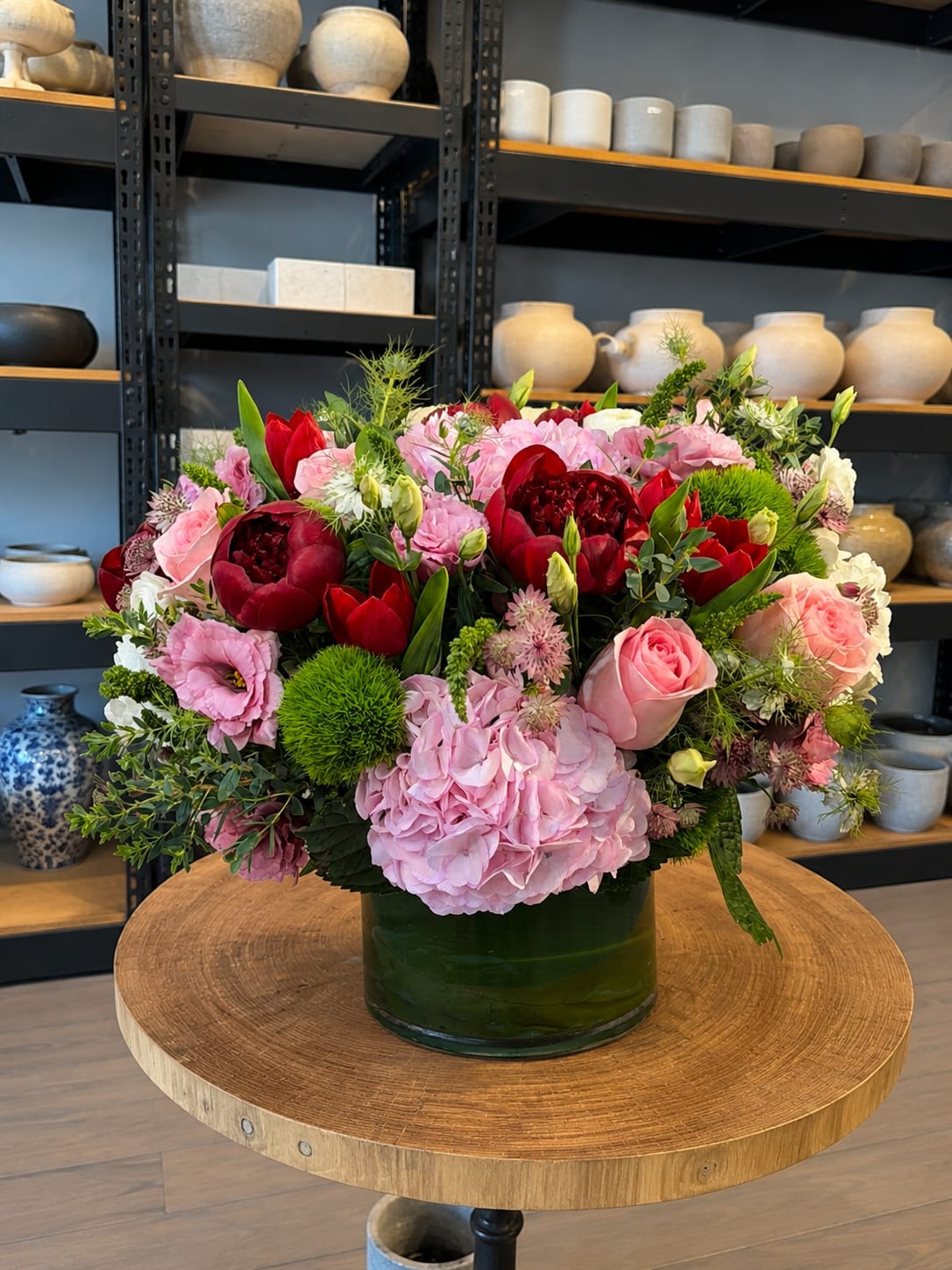 Mixed pink and red flower arrangement in a green glass vase
