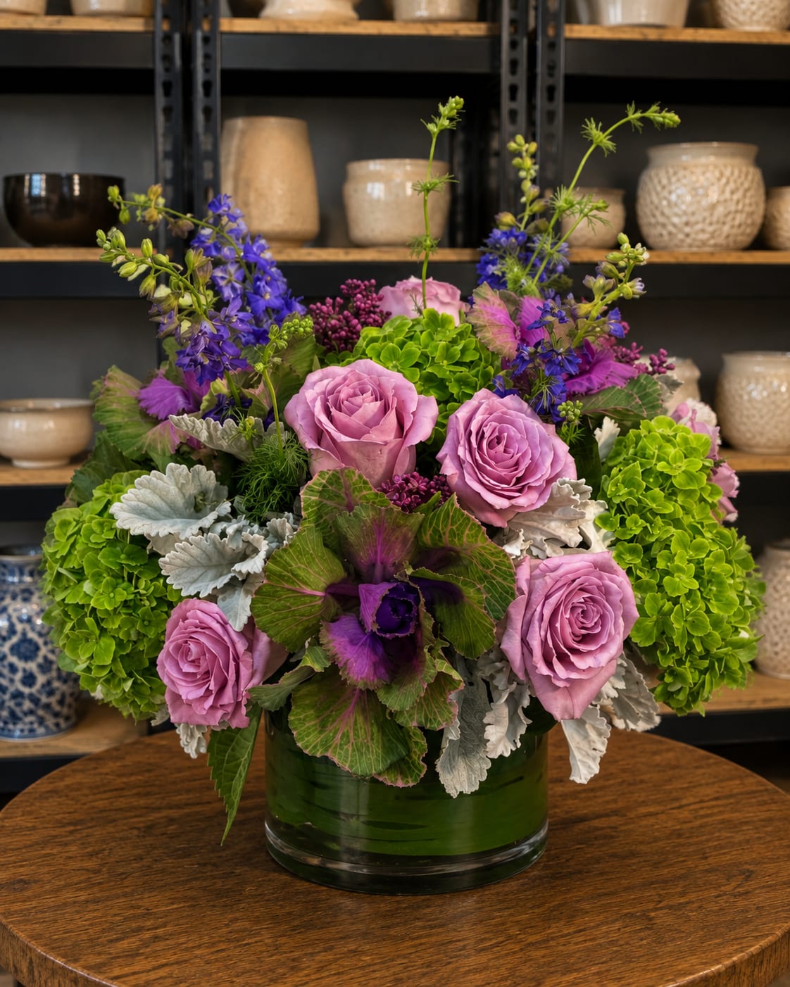Lavender roses and purple flowers in a green glass vase