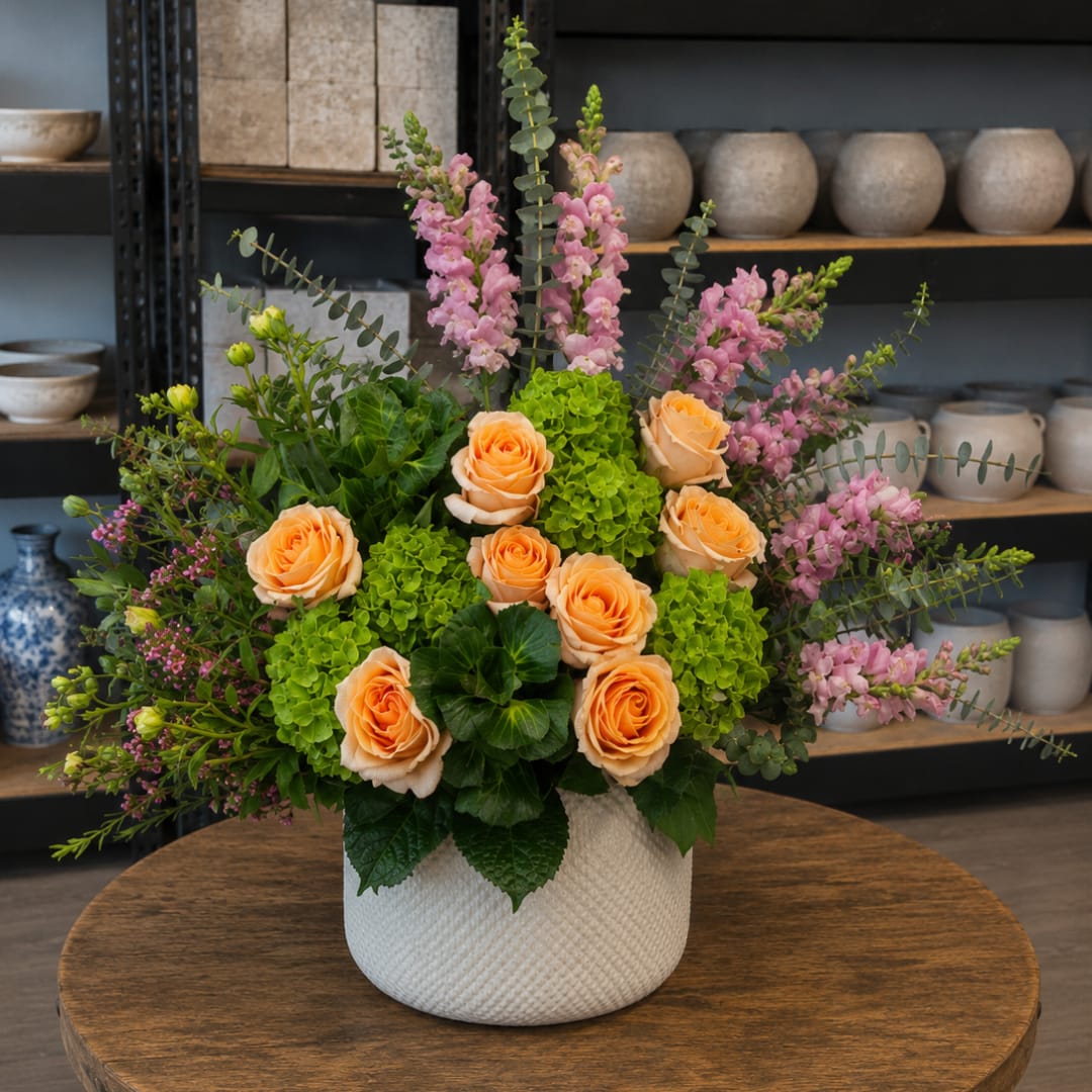 Peach roses and pink snapdragons in a white textured vase