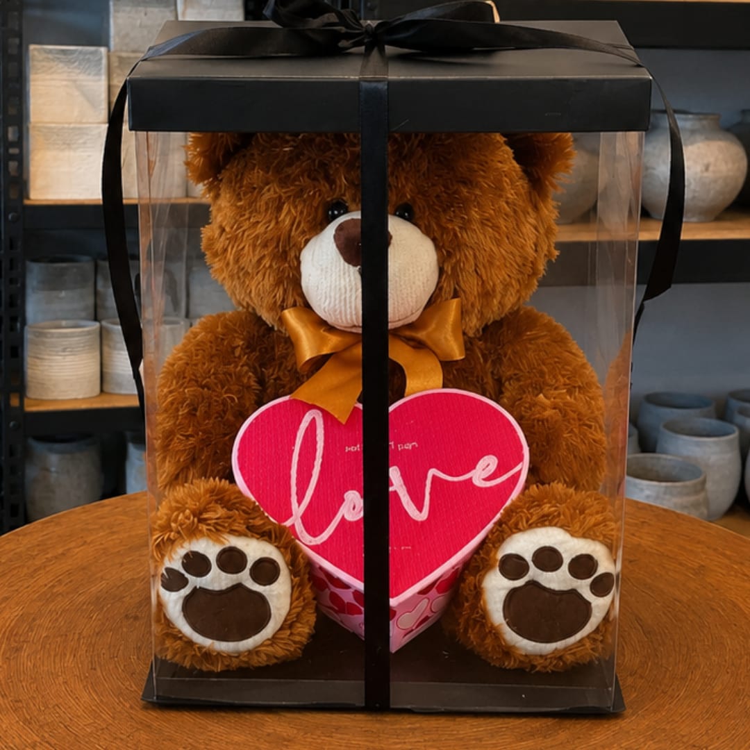 Teddy bear in a clear gift box holding a pink heart with "love" text