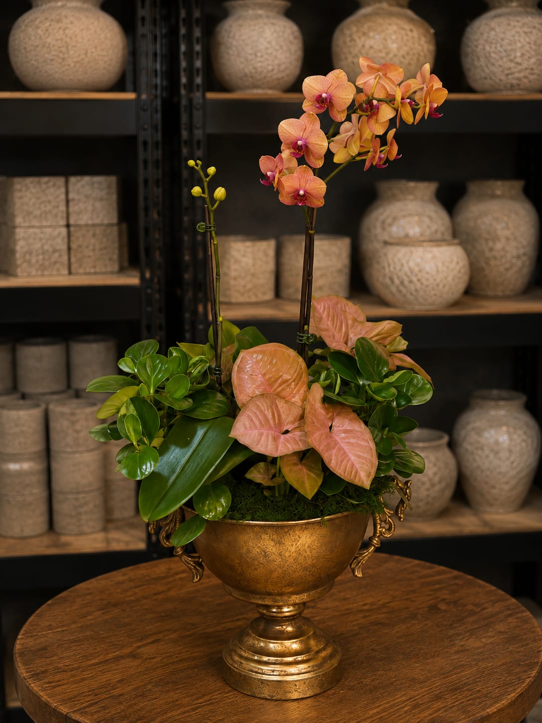 Orchid arrangement in a gold urn with pink leaves and green foliage