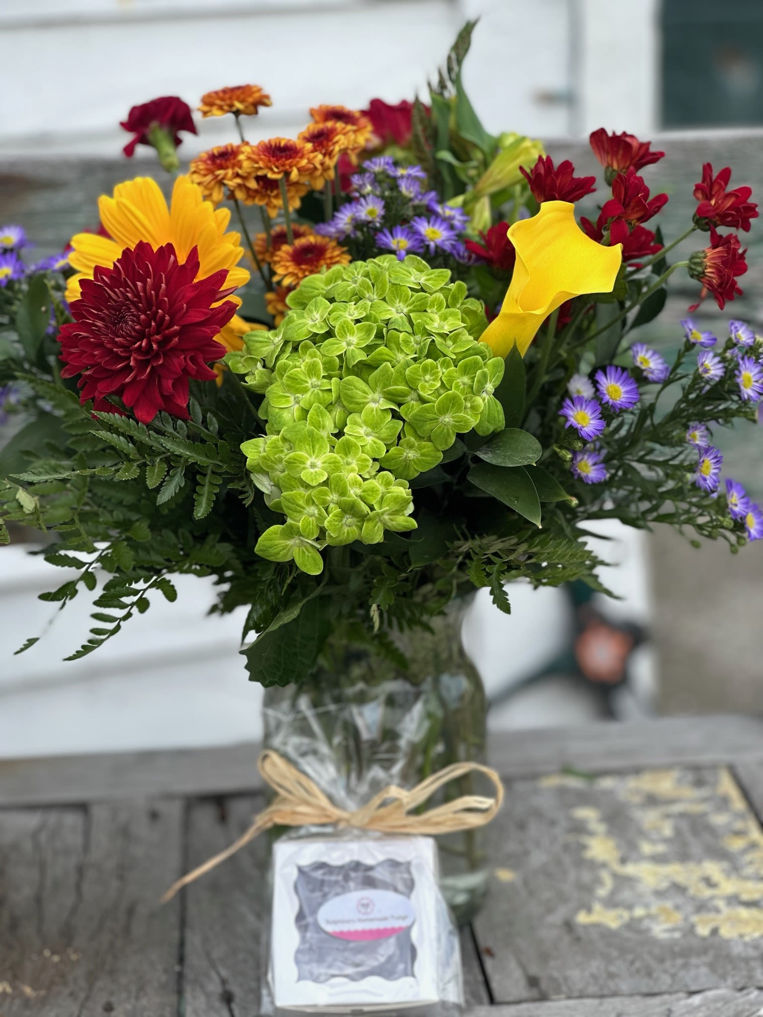 Deal of the day-Fall Surprise Bouquet - Deal of the day-Fall Surprise Bouquet with Ralphina's Homemade Fudge Green hydrangea, Yellow gerbera, Fell button poms and cushion mums, yellow calla lilies and purple monte arranged in a milk jug vase