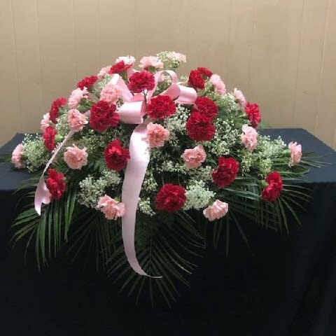Pink and red carnation arrangement with a ribbon on a table