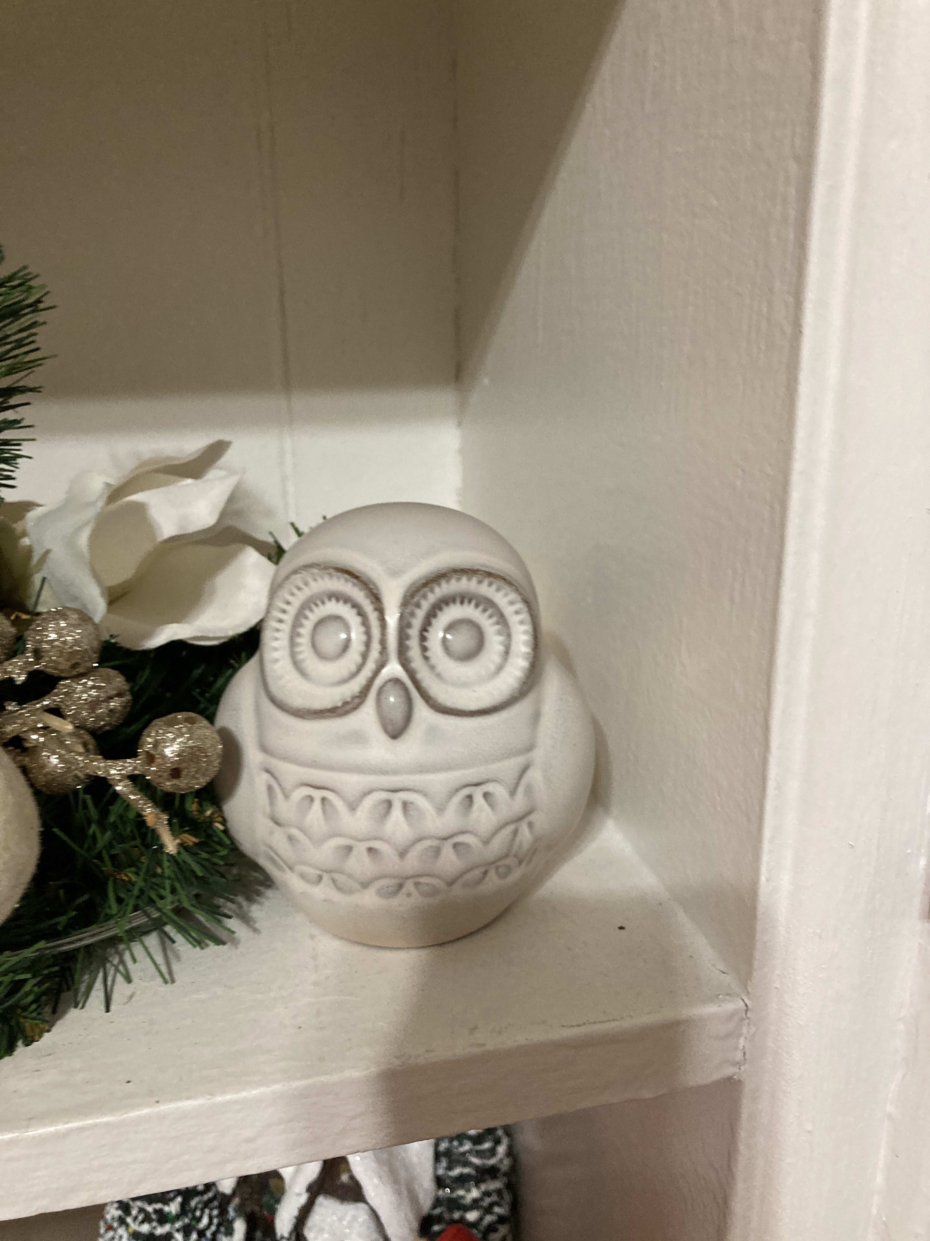 White ceramic owl figurine on a shelf beside holiday greenery