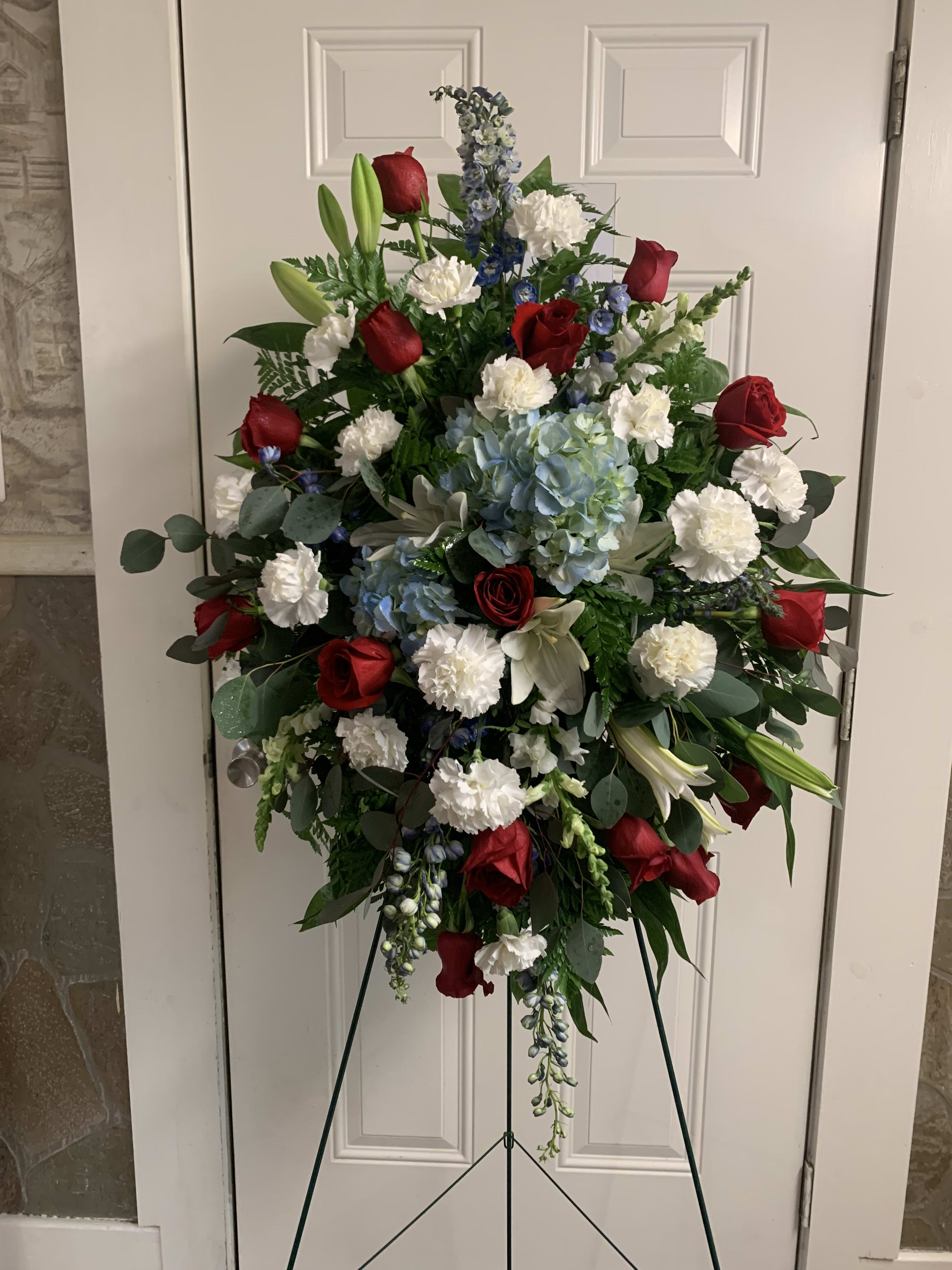 Standing floral spray with red roses, white carnations, and blue flowers