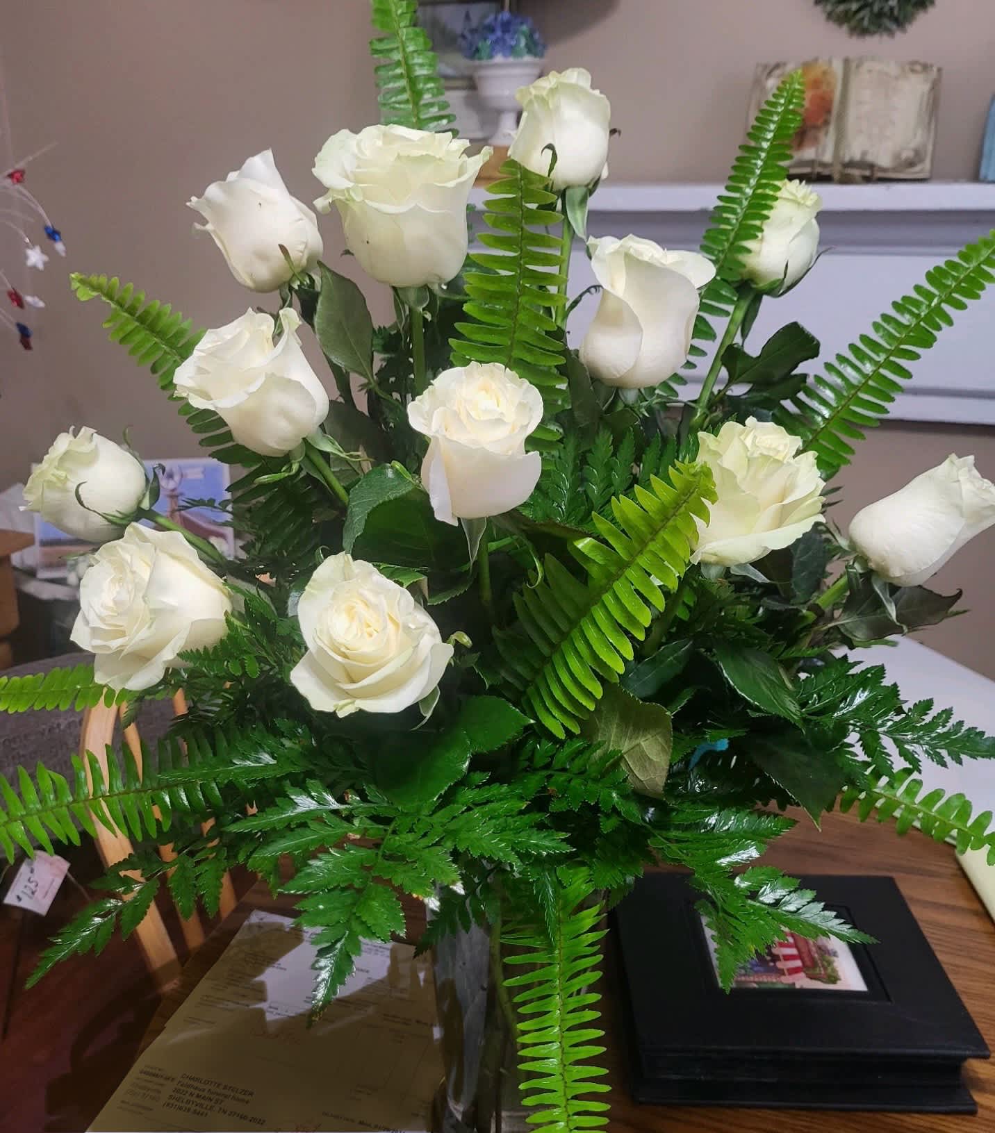 White roses arranged with fern foliage in a clear vase