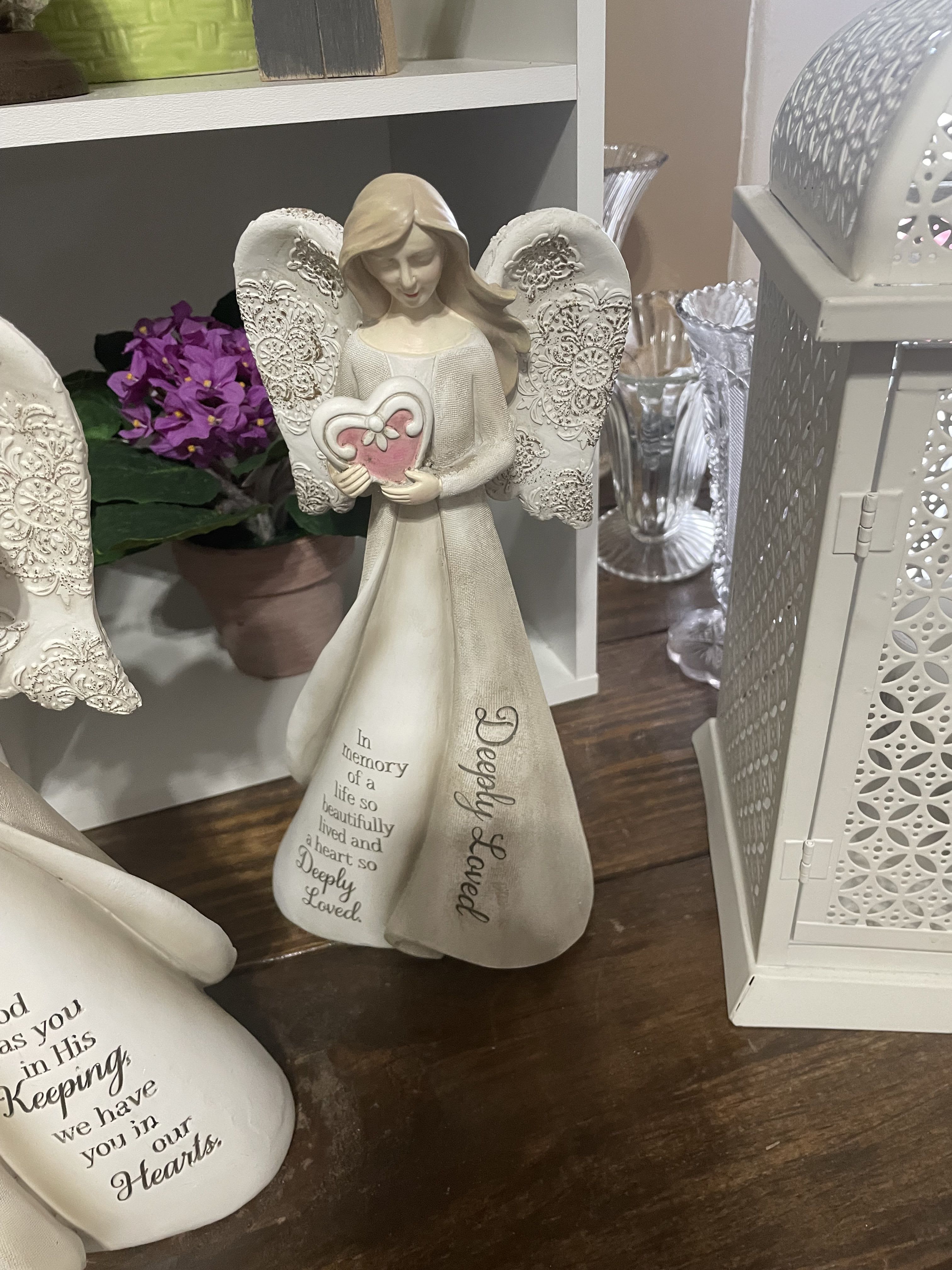 Decorative angel figurine with a heart, beside a small purple flower arrangement.