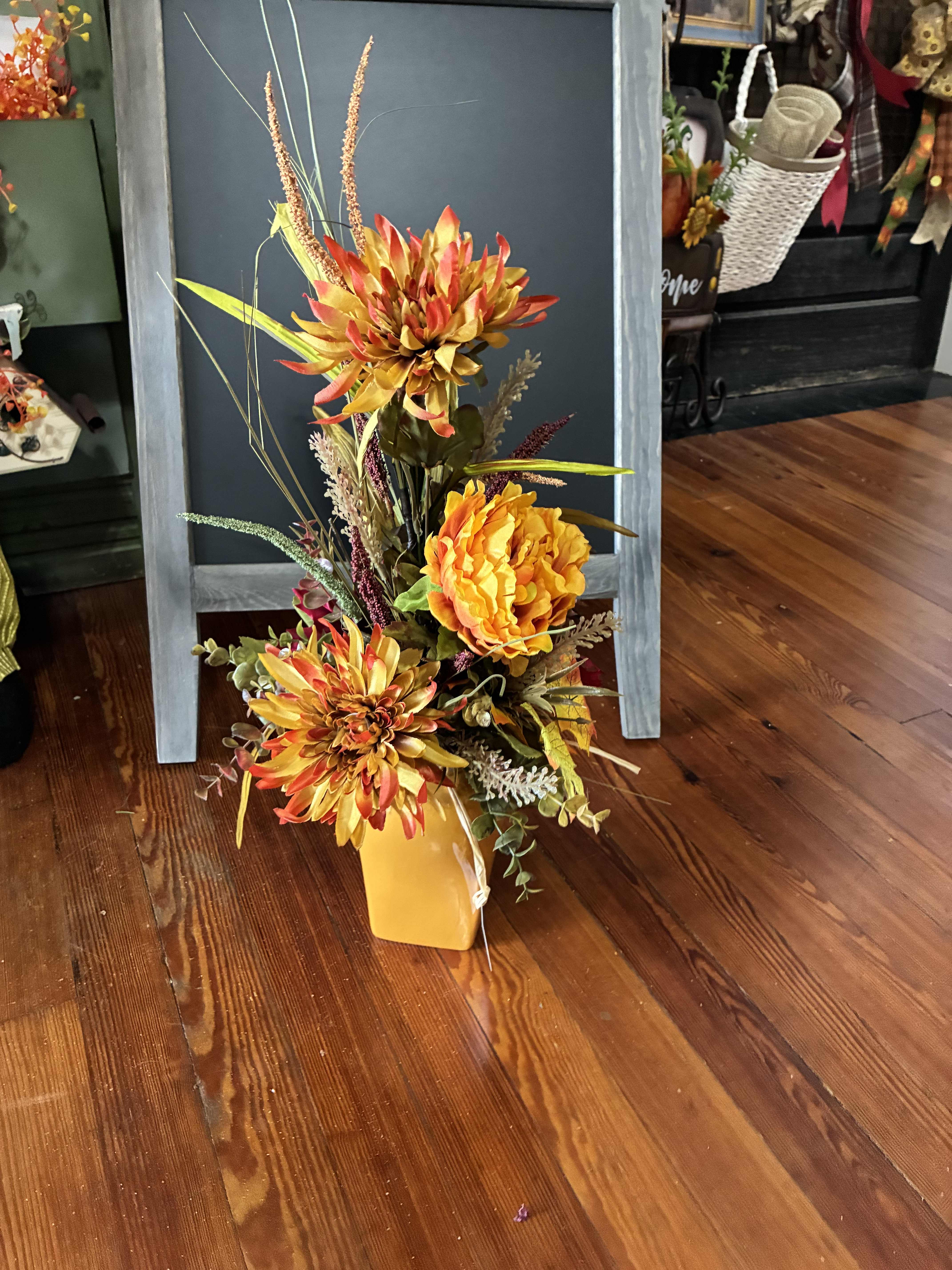 Tall autumn floral arrangement in a yellow vase with orange blooms