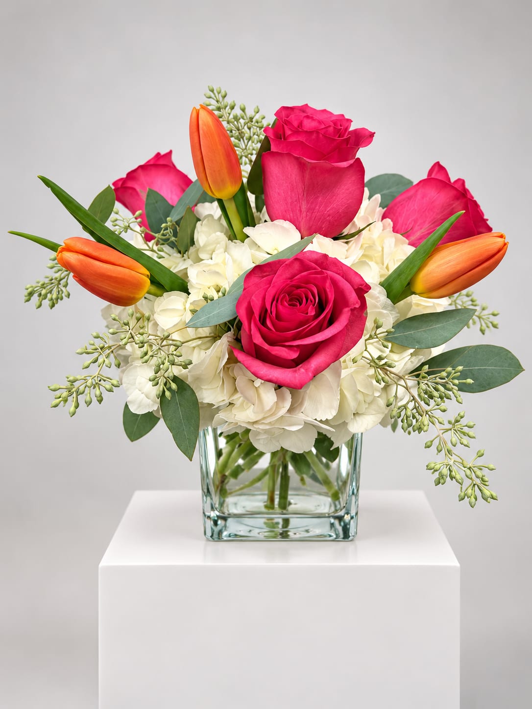 Pink roses and orange tulips in a clear glass vase