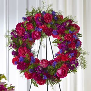 Heart-shaped floral wreath with pink roses and purple flowers on a stand