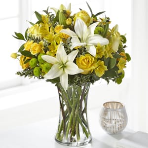 Yellow and white bouquet with lilies and roses arranged in a clear glass vase