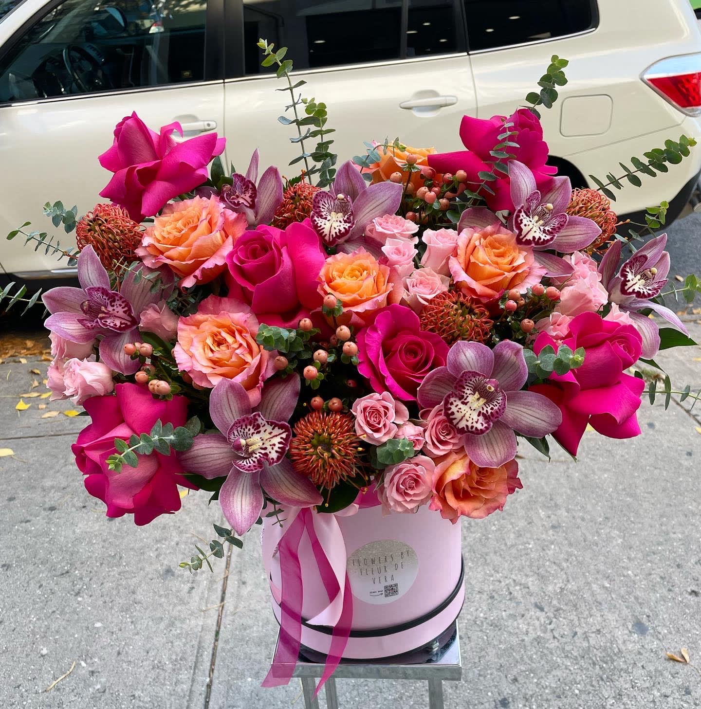 Pink and peach roses with purple orchids in a pink hatbox