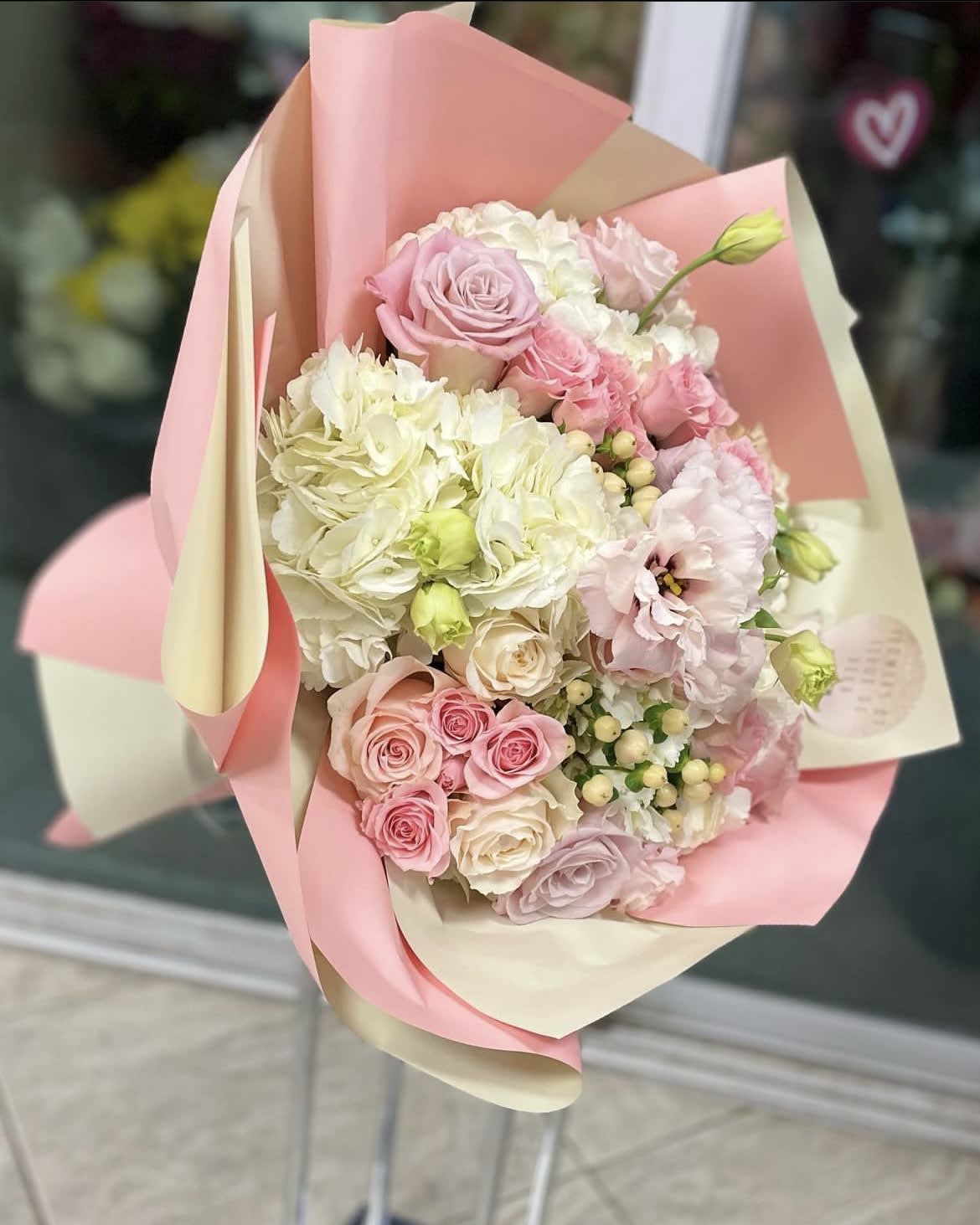 Pink and white bouquet of roses, hydrangeas, and lisianthus in pastel wrap