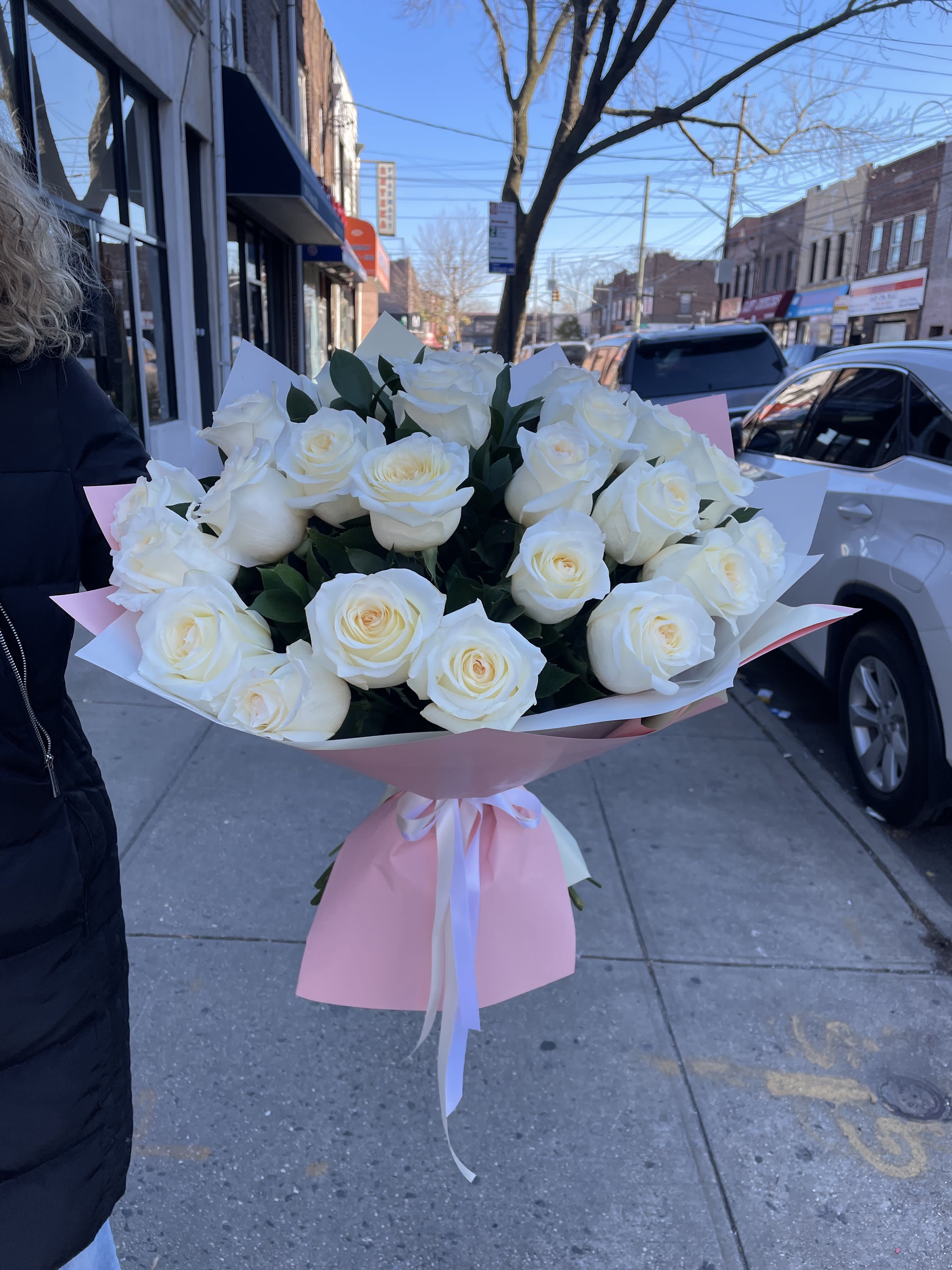 Large bouquet of white roses wrapped in pink paper with ribbon