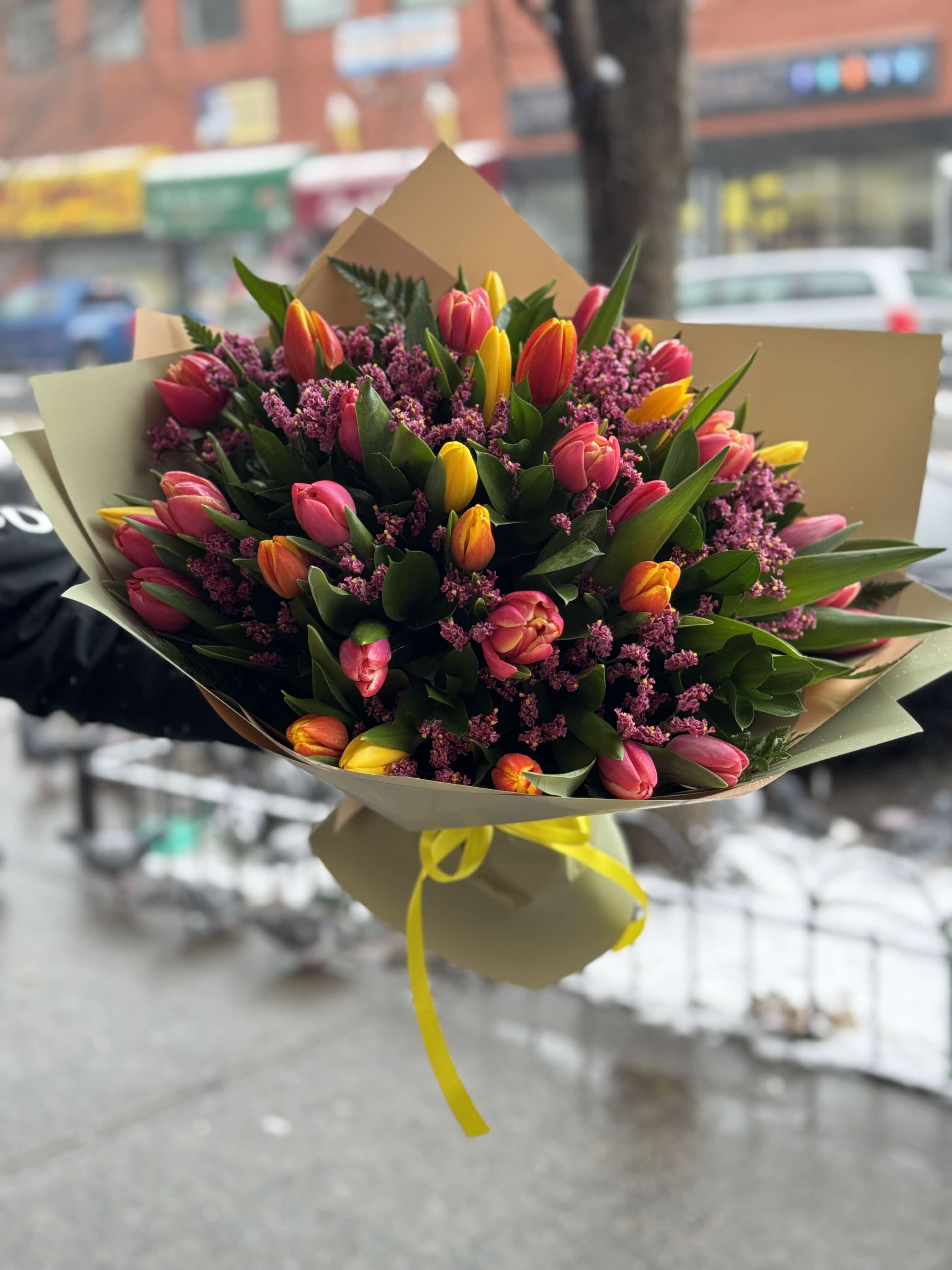 Bouquet of pink and yellow tulips wrapped in paper with a yellow ribbon