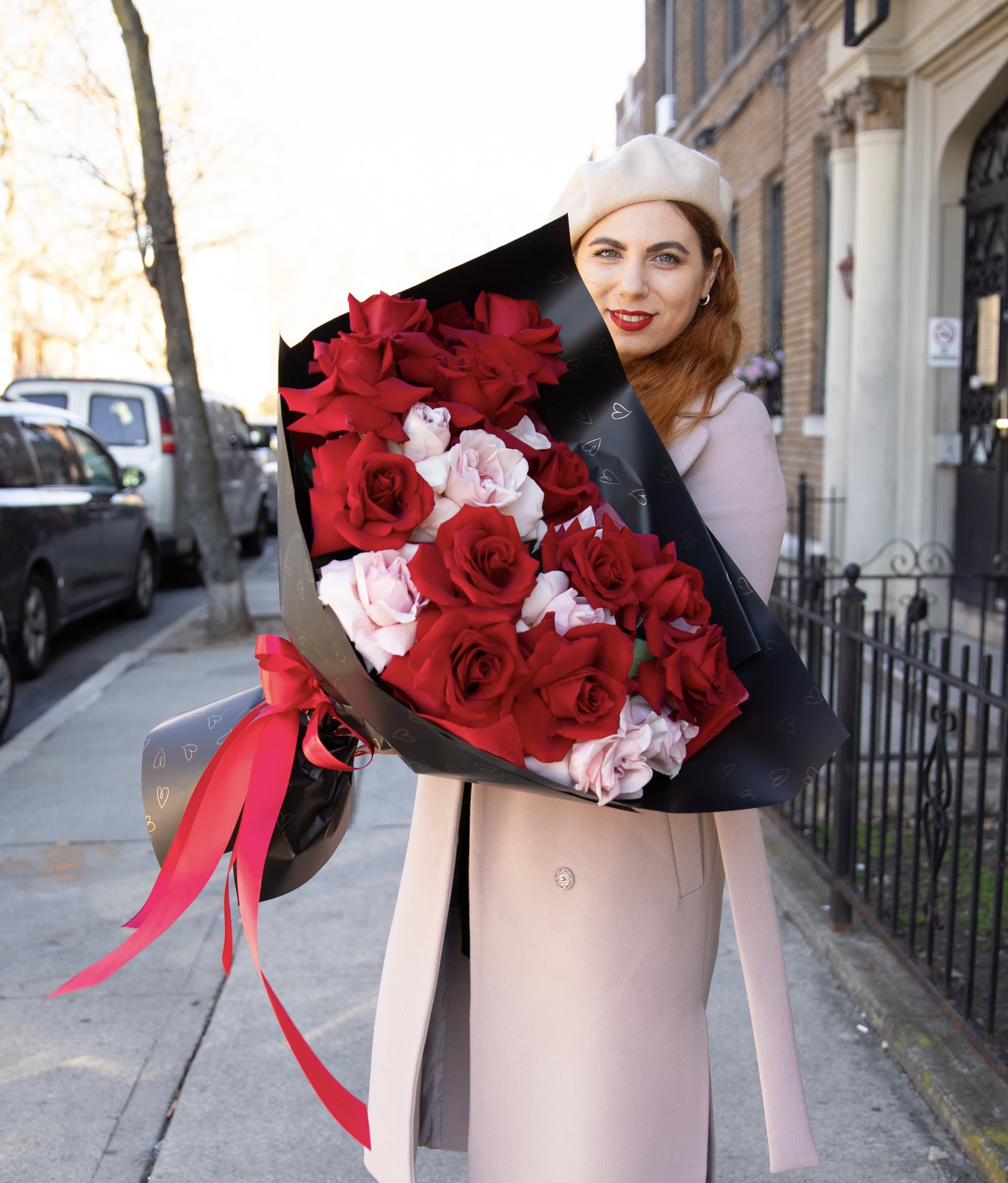 Woman holding a large bouquet of red and pale pink roses wrapped in black paper