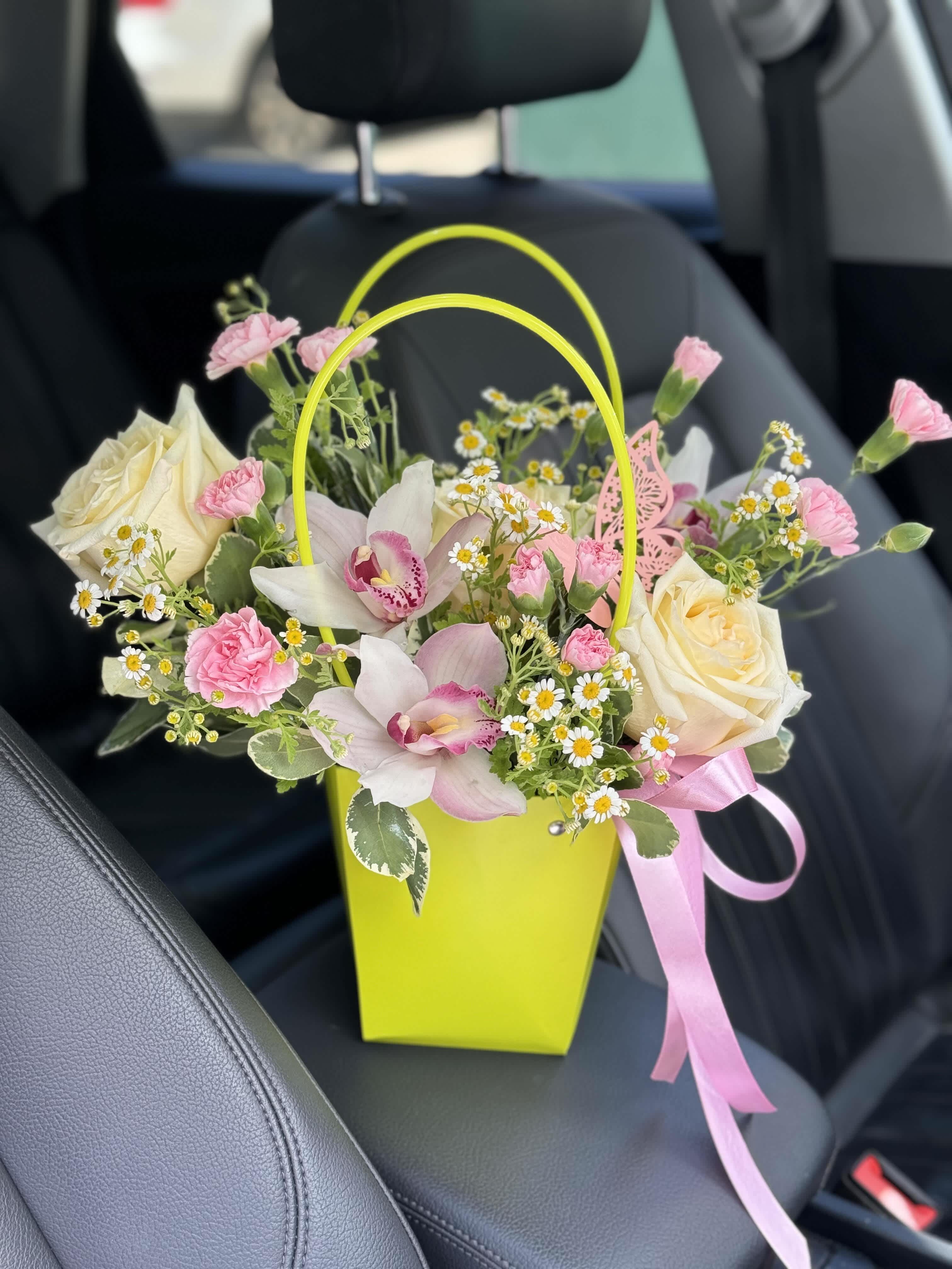 Pink and cream flowers in a bright yellow gift bag with a pink ribbon