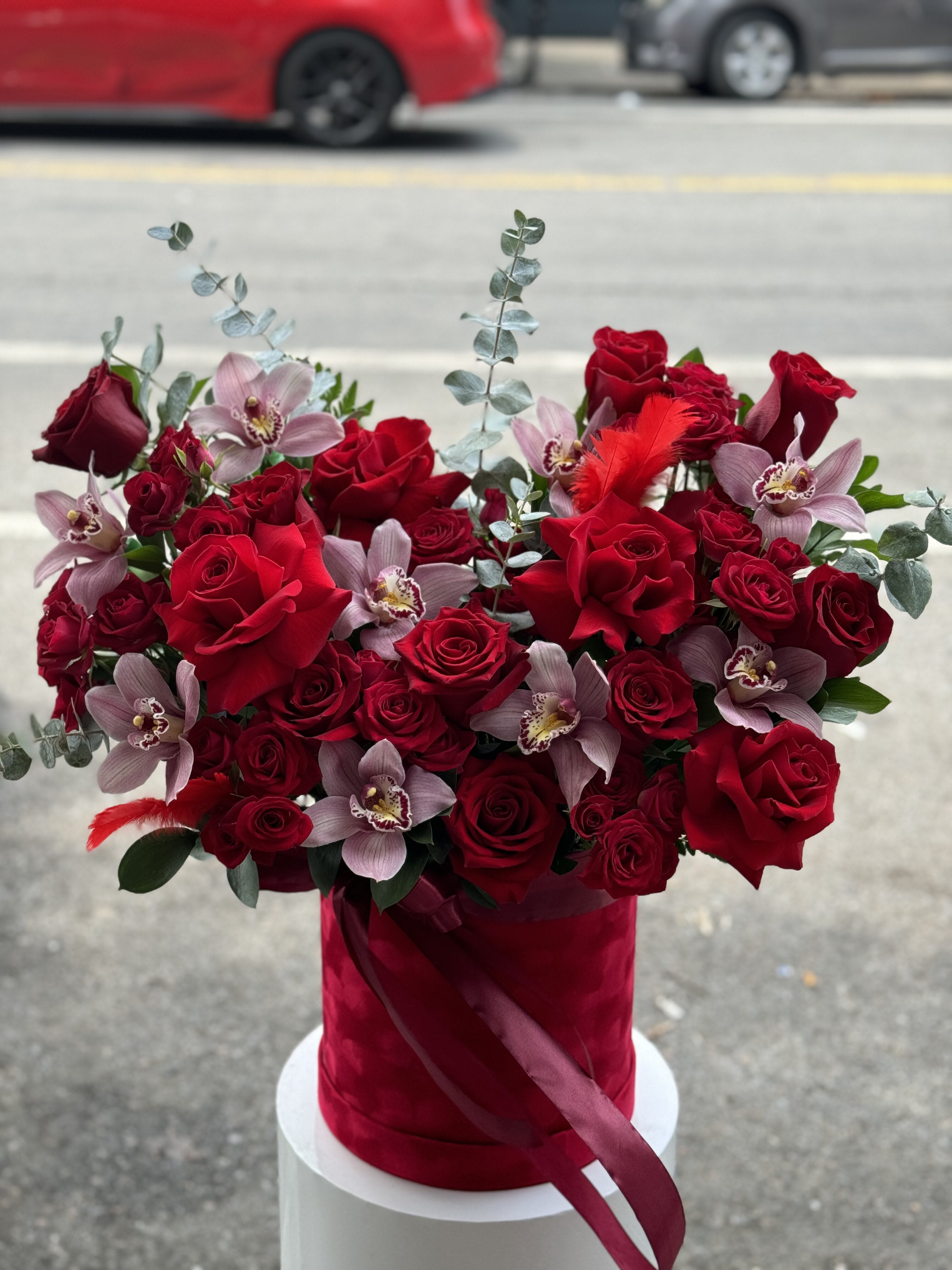 Red roses and pale orchids arranged in a red hat box