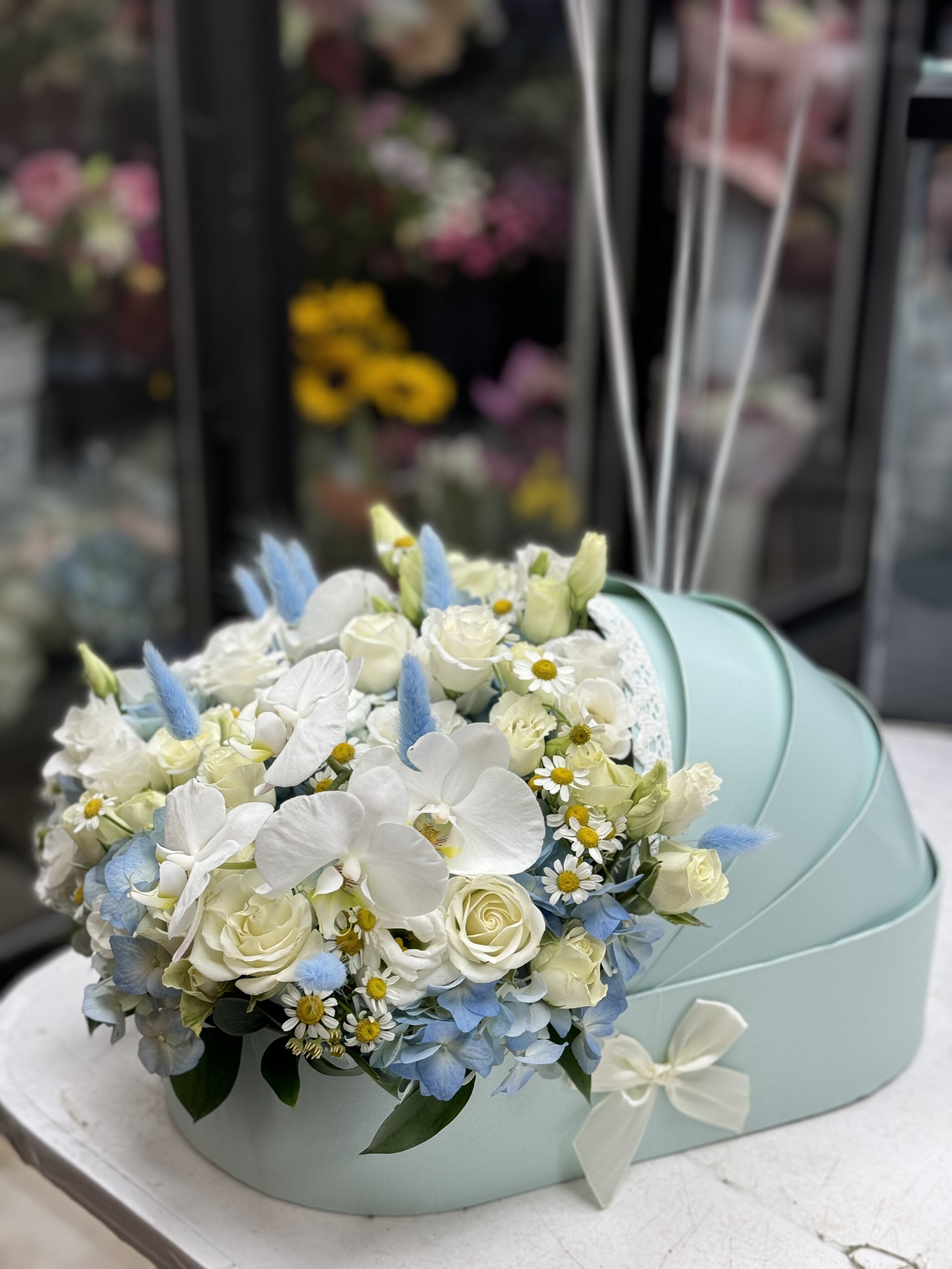 White and pale blue floral arrangement in a mint gift box