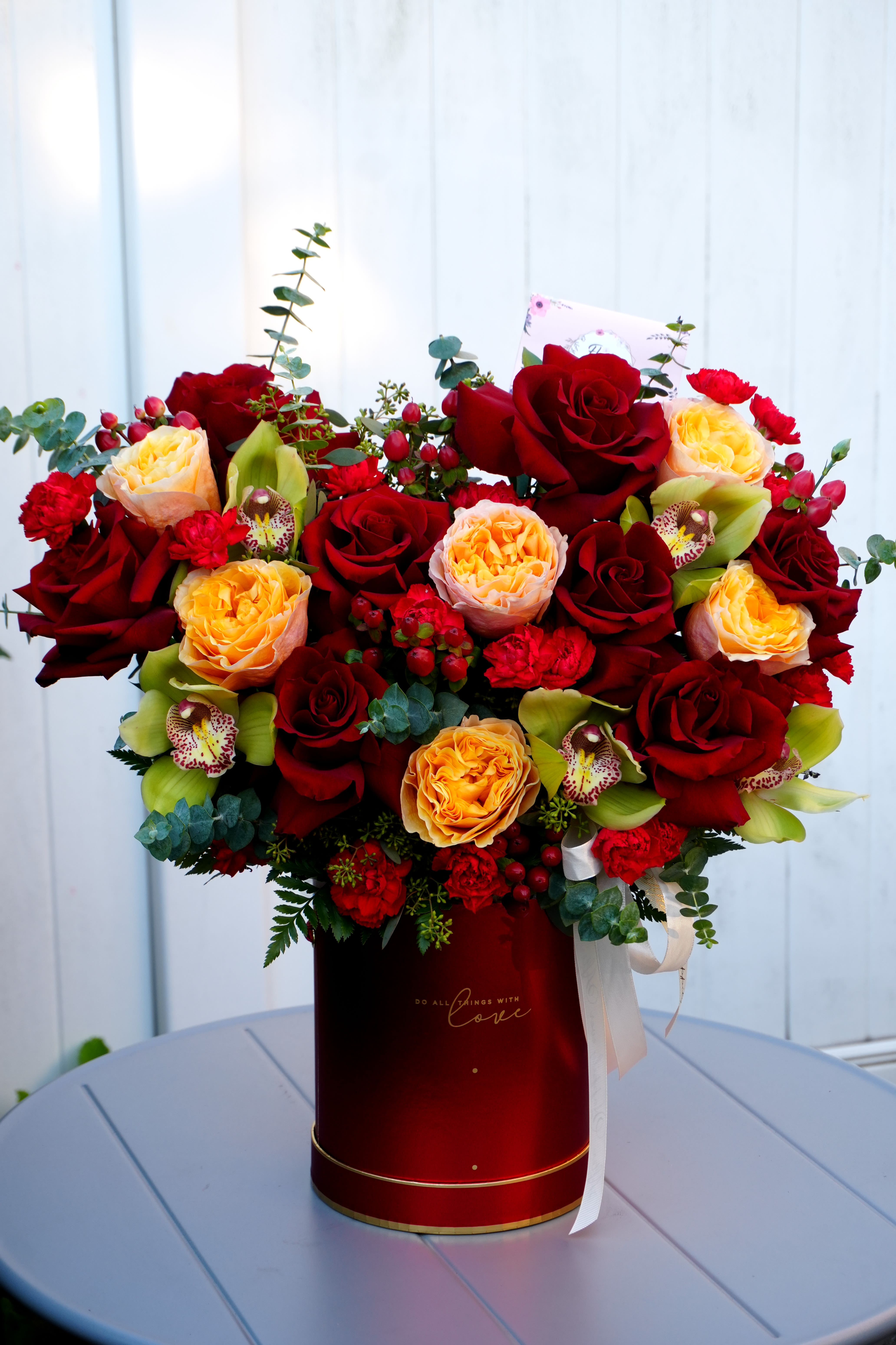 Red and peach roses arranged in a tall red box with ribbon