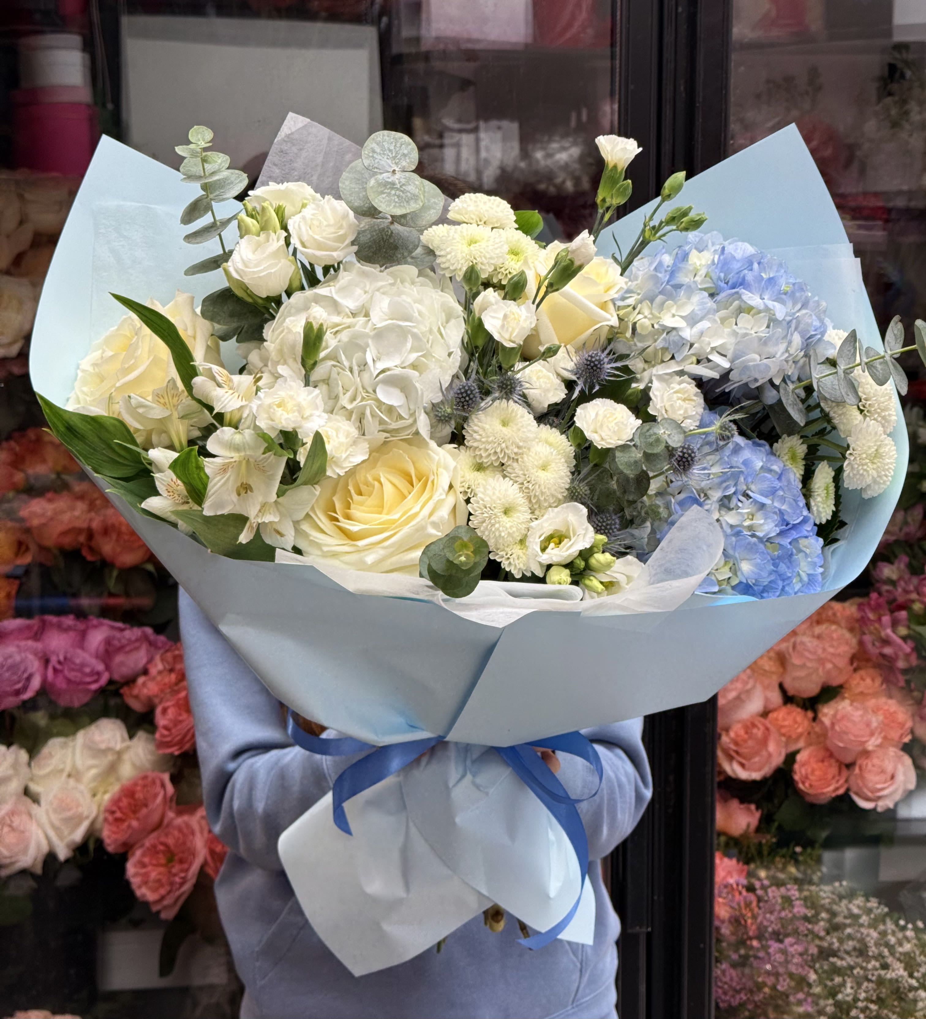 Large bouquet of white and pale blue flowers wrapped in light blue paper