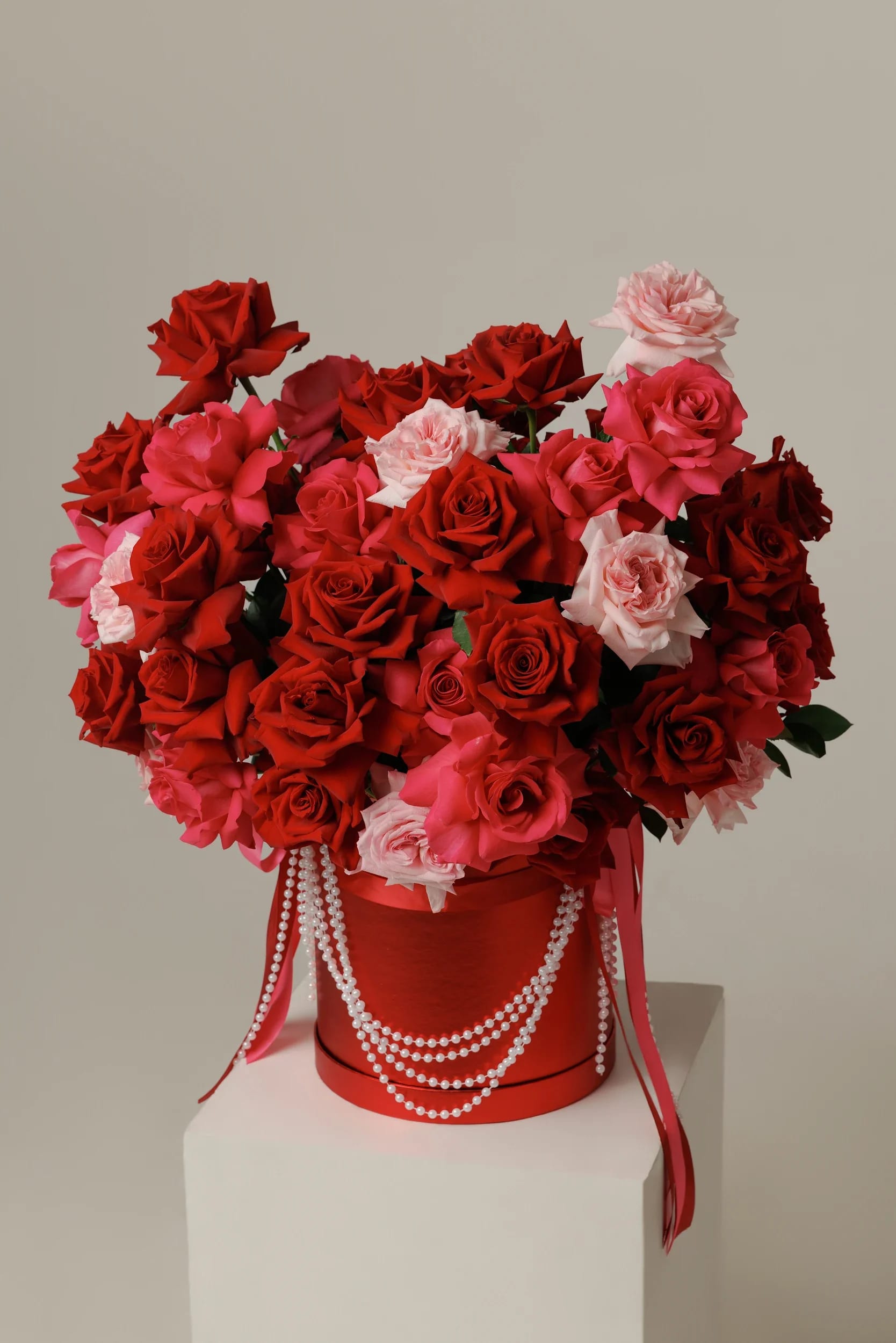 Large bouquet of red and pink roses in a red hatbox with pearl strands
