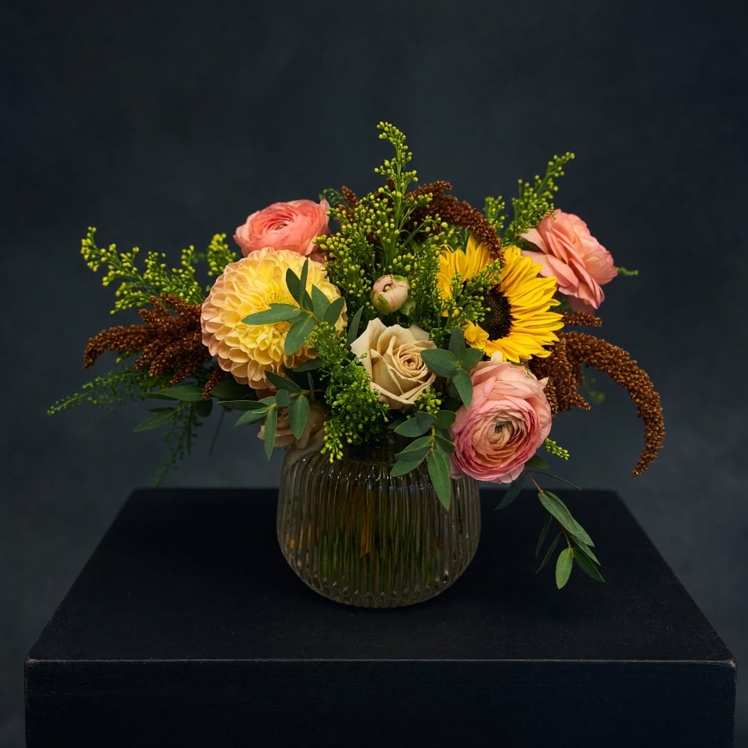 Mixed bouquet of pink, yellow, and cream flowers in a ribbed glass vase