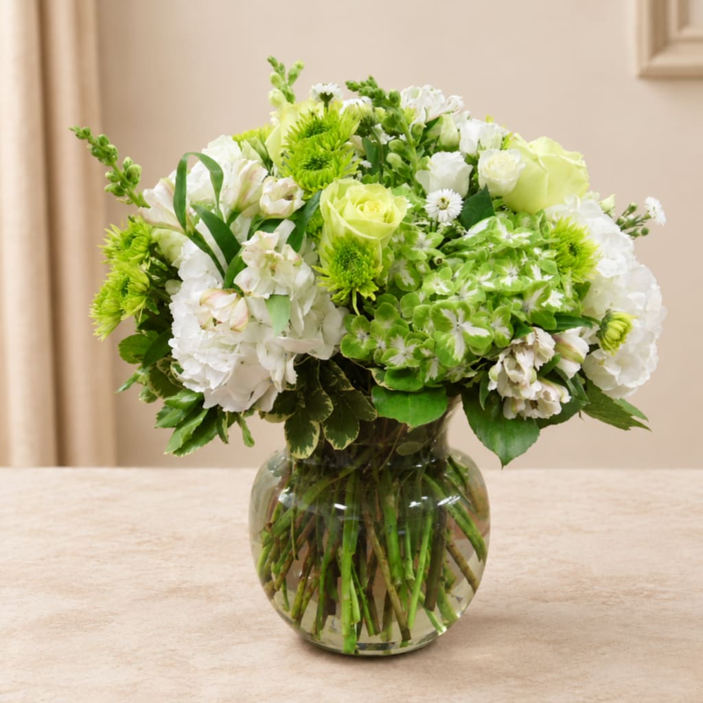 Green and white flower arrangement in a round glass vase