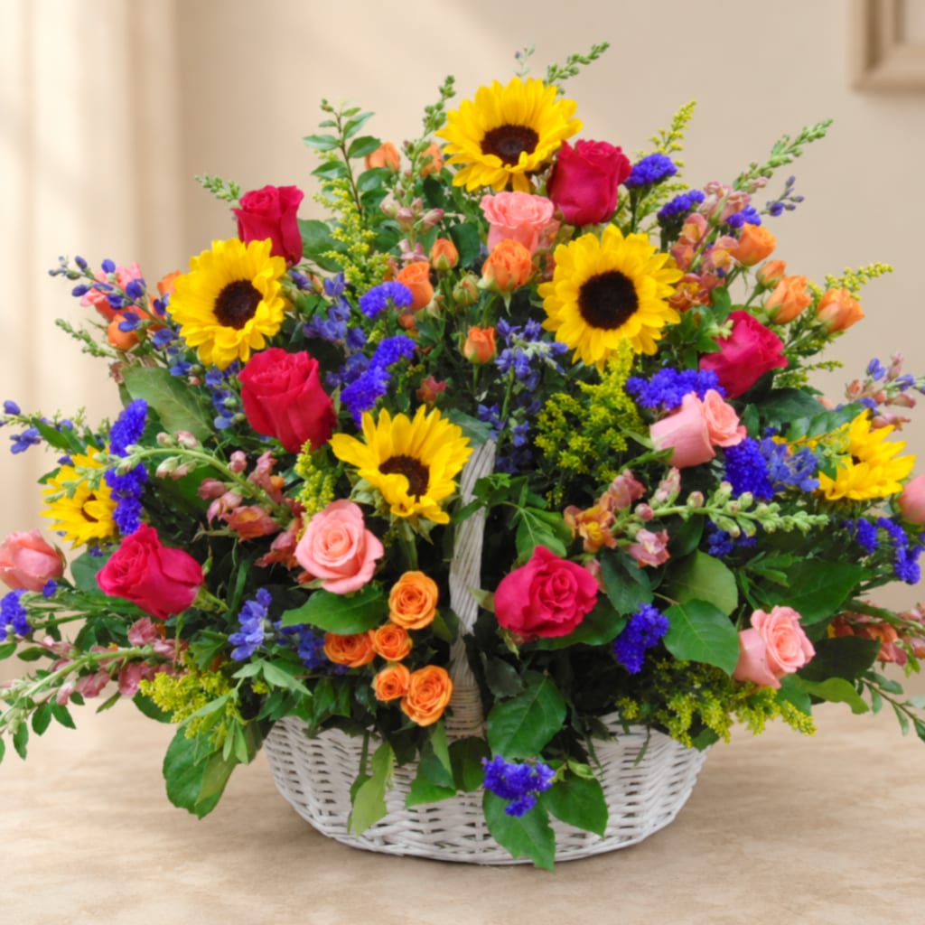 Mixed bouquet of sunflowers, roses, and purple flowers in a white basket