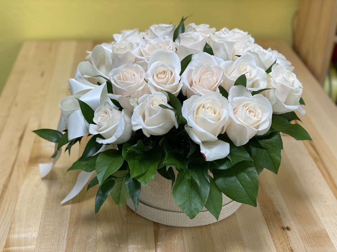 Round arrangement of white roses in a beige box with a white ribbon