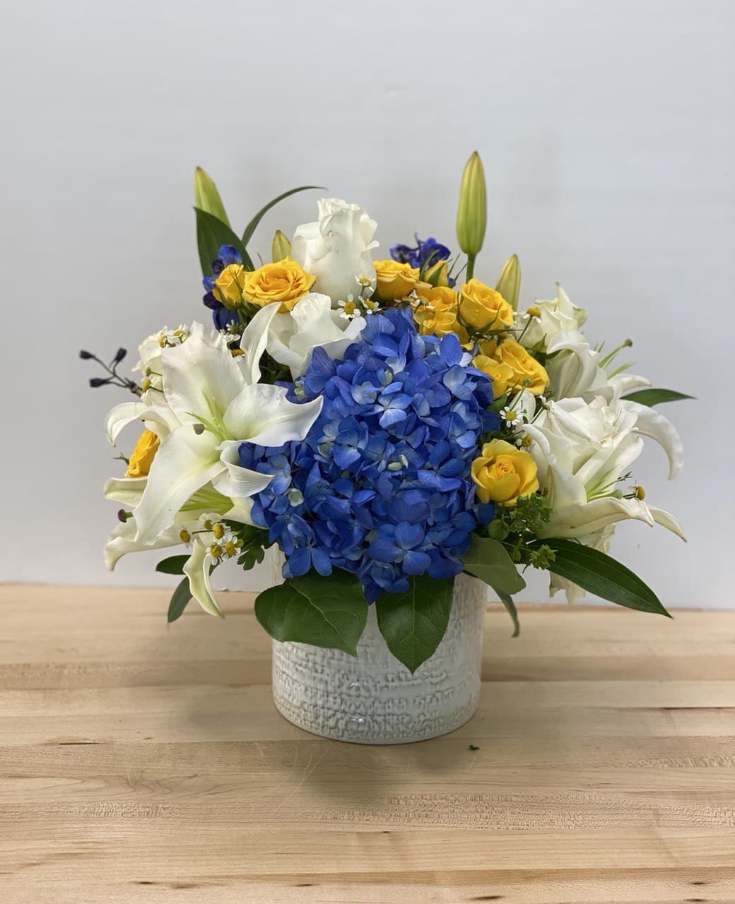 Blue hydrangea and white lilies with yellow roses in a white vase