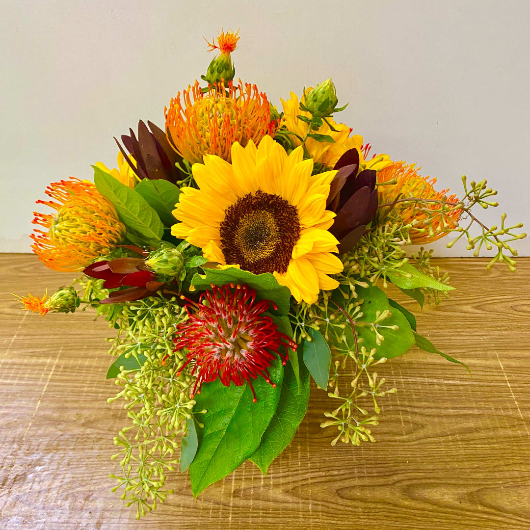 Sunflower bouquet with orange and red pincushion blooms on a wooden surface