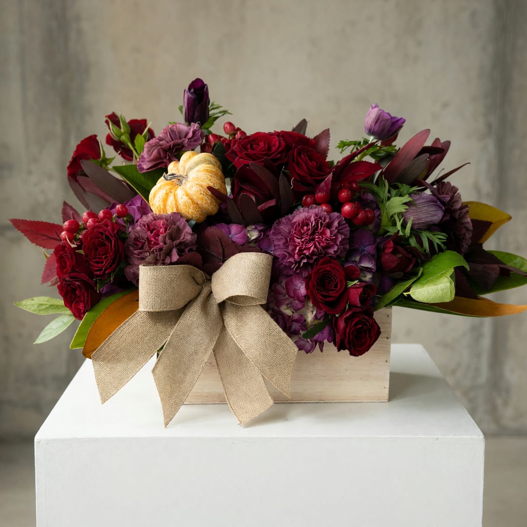 Red and purple floral arrangement in a wooden box with a burlap bow