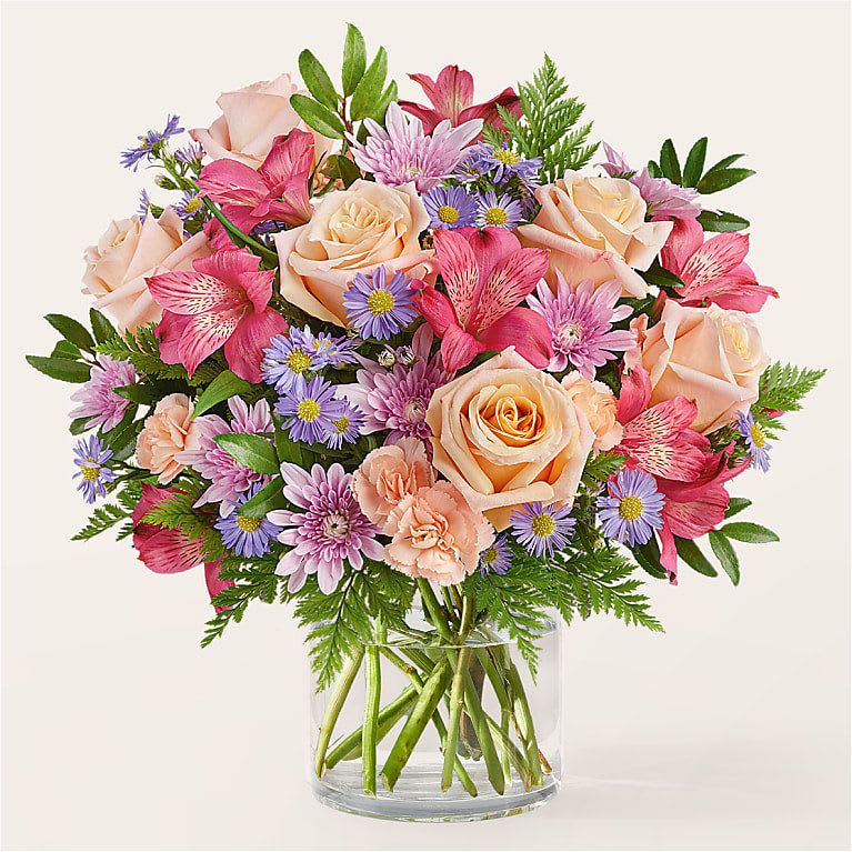 Bouquet of peach roses, pink lilies, and purple daisies in a glass vase